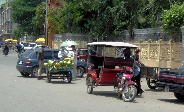 Tuk-tuk rouge et charrette de noix de coco vertes dans une rue de Phnom Penh