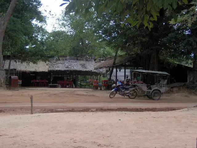 Gargotes aux toits de chaume et tuk-tuk sur une piste de terre ombragée au Cambodge