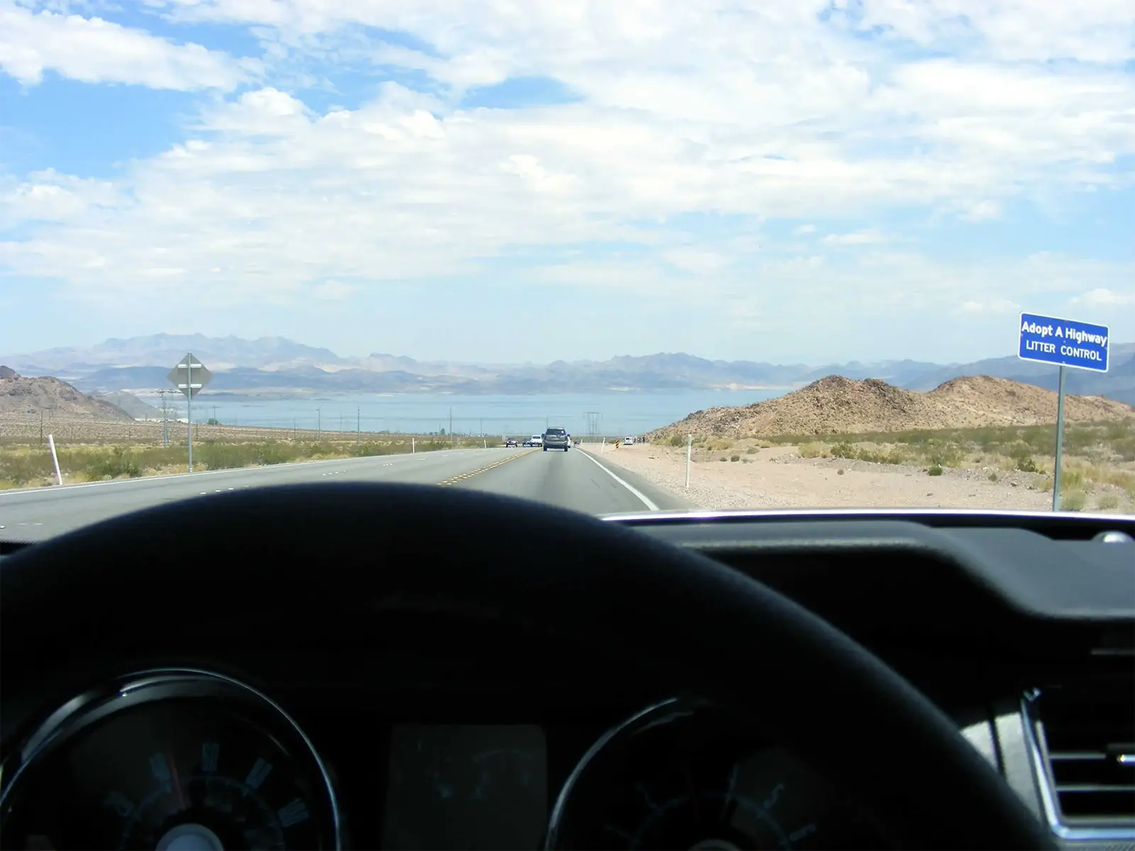 Route du désert qui plonge vers un grand lac, vue depuis le volant d’une Ford Mustang dans l’Ouest américain