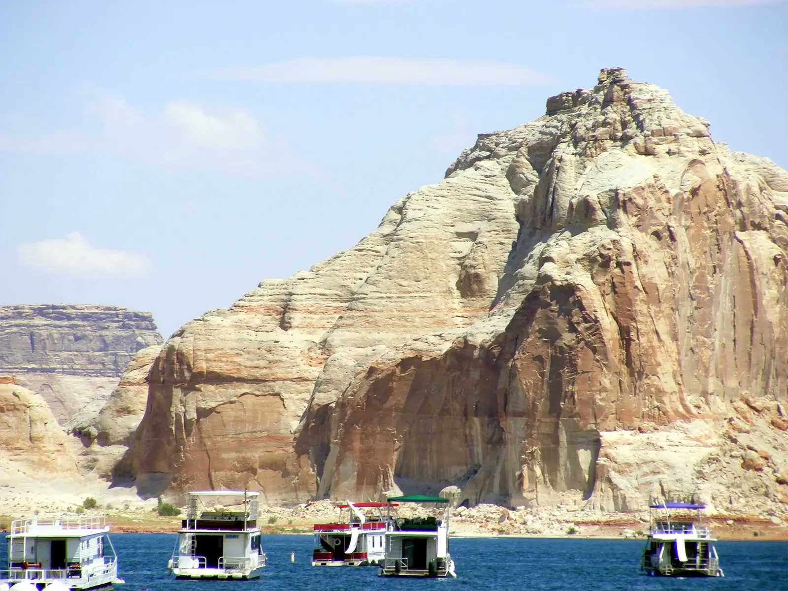 Bateaux-maisons amarrés devant une imposante butte de grès blanc et rouge sur le lac Powell