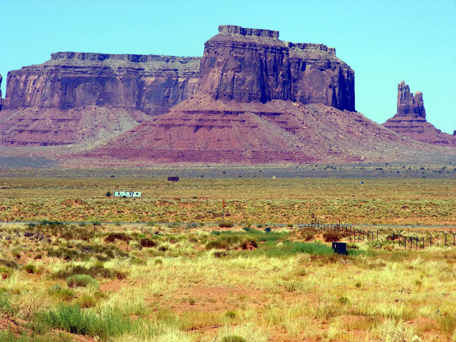 Buttes de grès rouge et aiguille rocheuse au-dessus de la plaine herbeuse, sur la route de Monument Valley