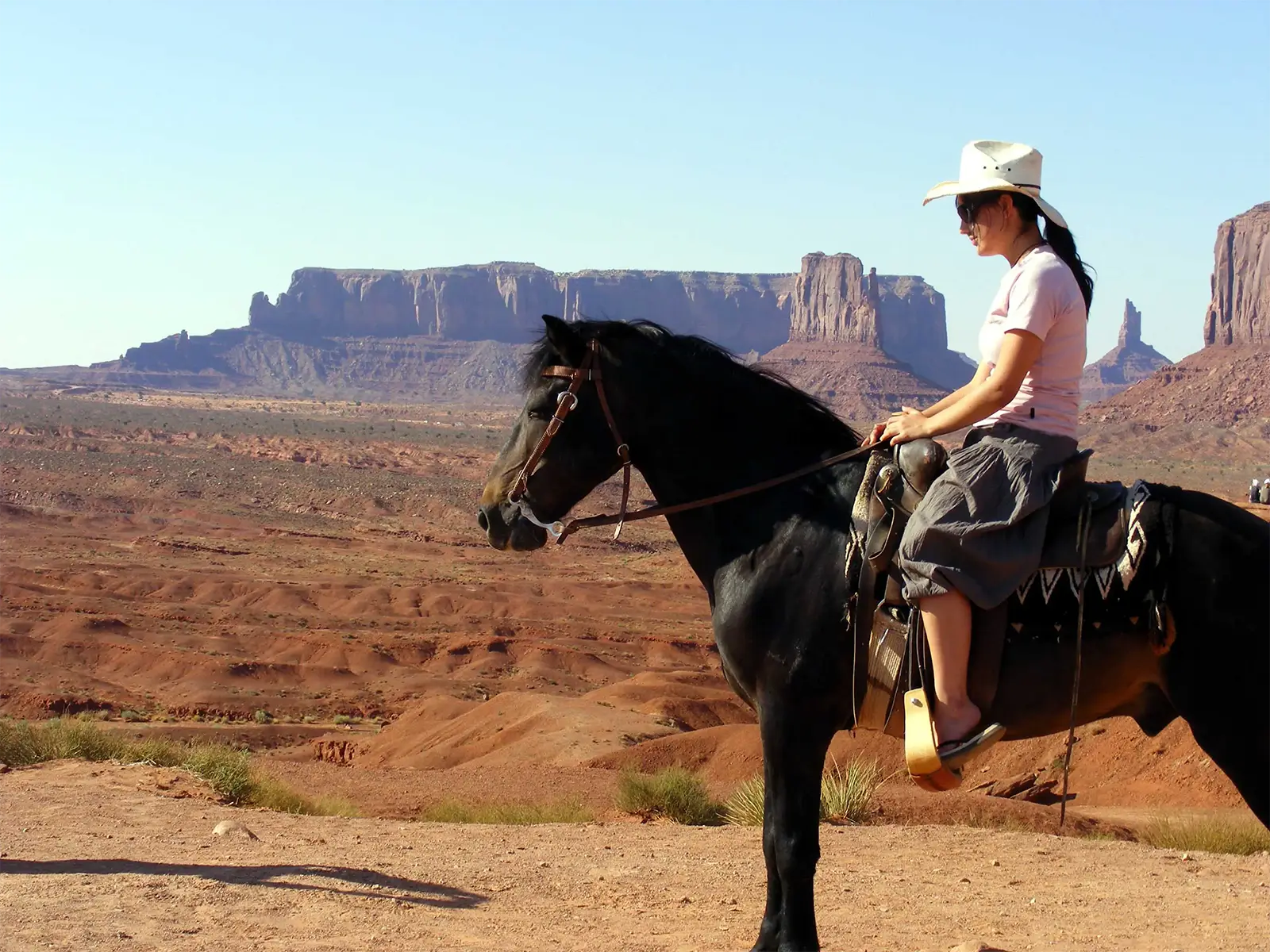 Cavalière au chapeau de cowboy sur un cheval noir face aux mesas de Monument Valley