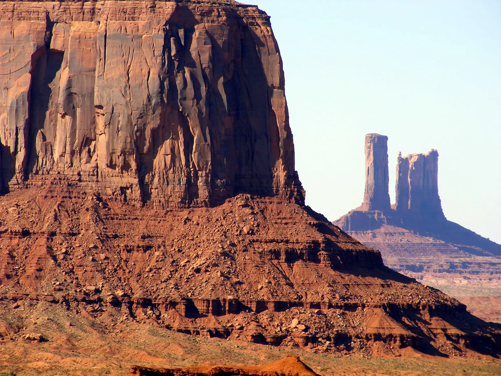 Gros plan sur la paroi érodée d’une butte de grès et deux pinacles à l’arrière-plan, à Monument Valley