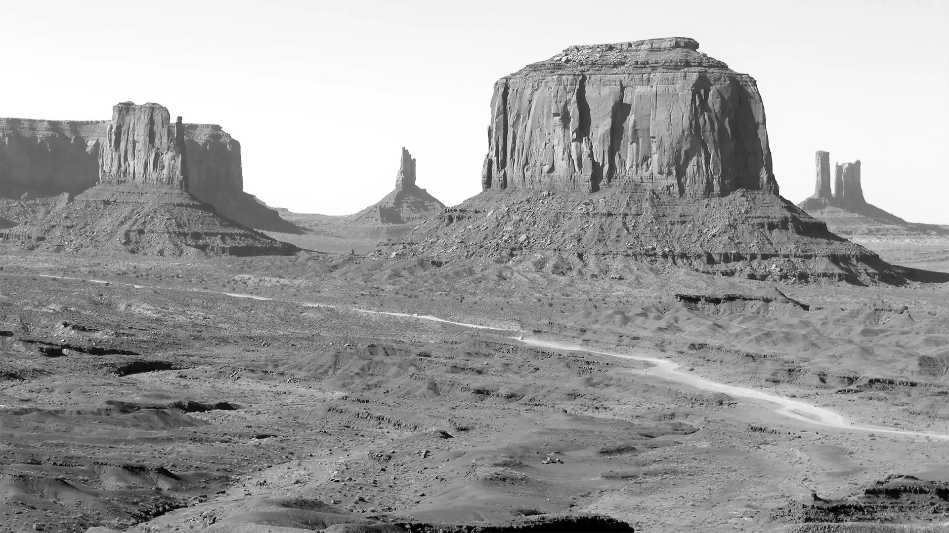 La vallée et ses buttes en noir et blanc, traversées par une piste de terre à Monument Valley