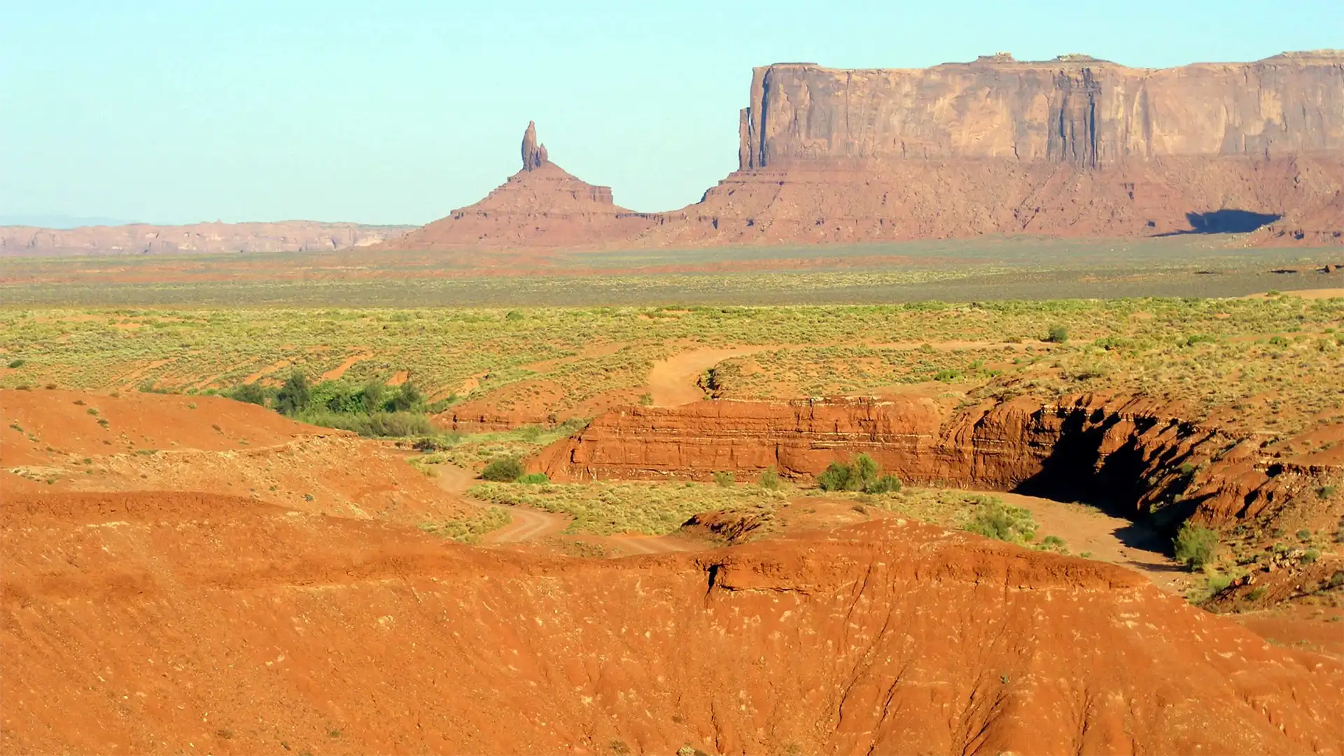Aiguille rocheuse et grande mesa au-dessus des ravines de sable rouge de Monument Valley