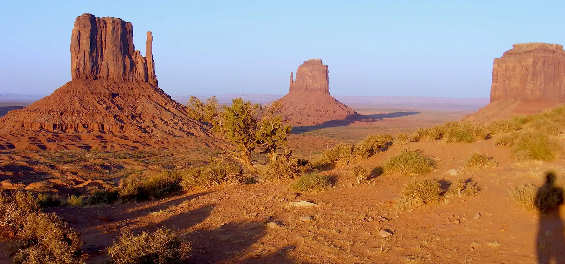 Les Mittens et Merrick Butte au coucher du soleil, avec l’ombre d’un voyageur, à Monument Valley