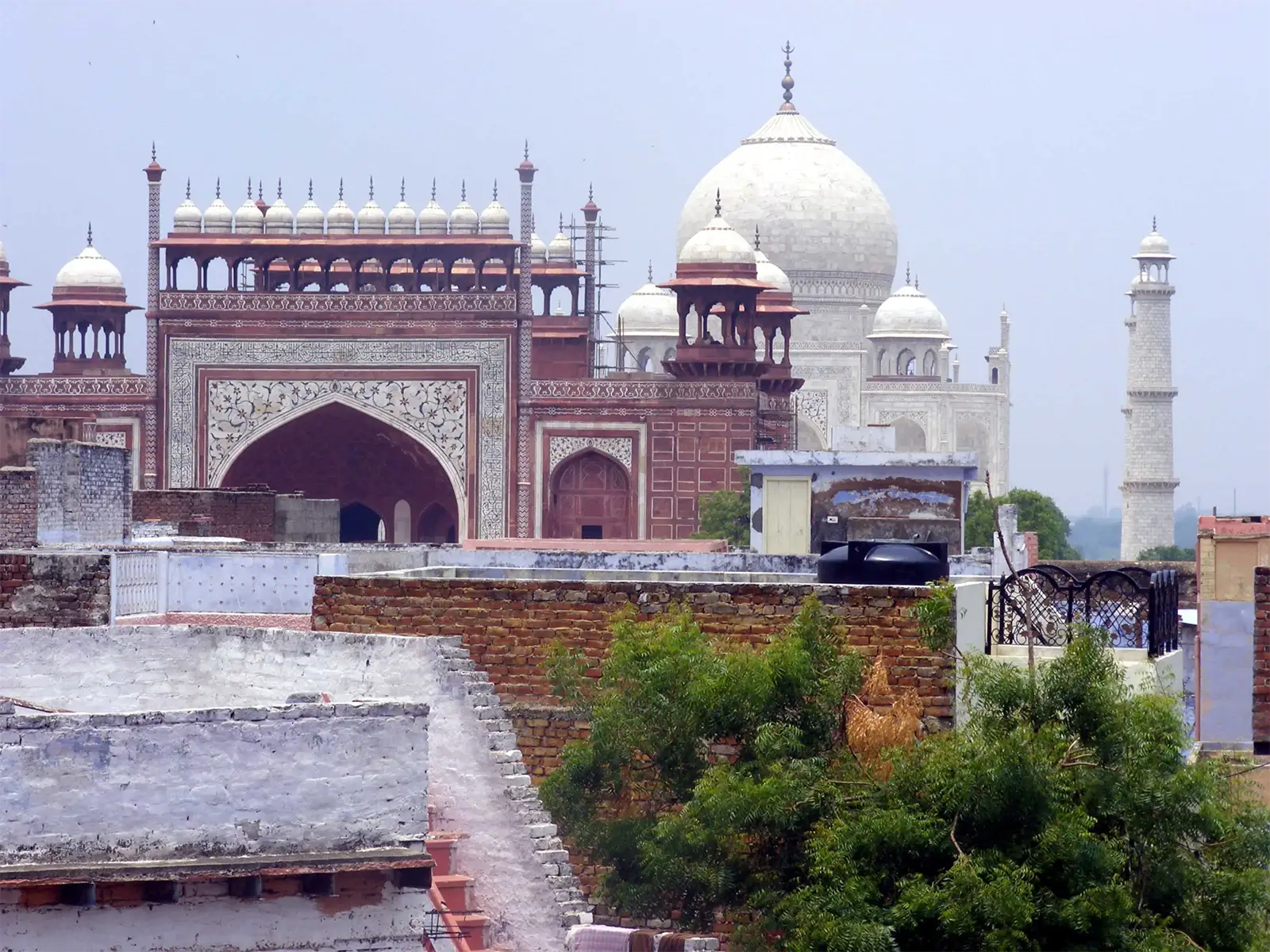 La grande porte en grès rouge du Taj Mahal et son dôme blanc au-dessus des toits d’Agra