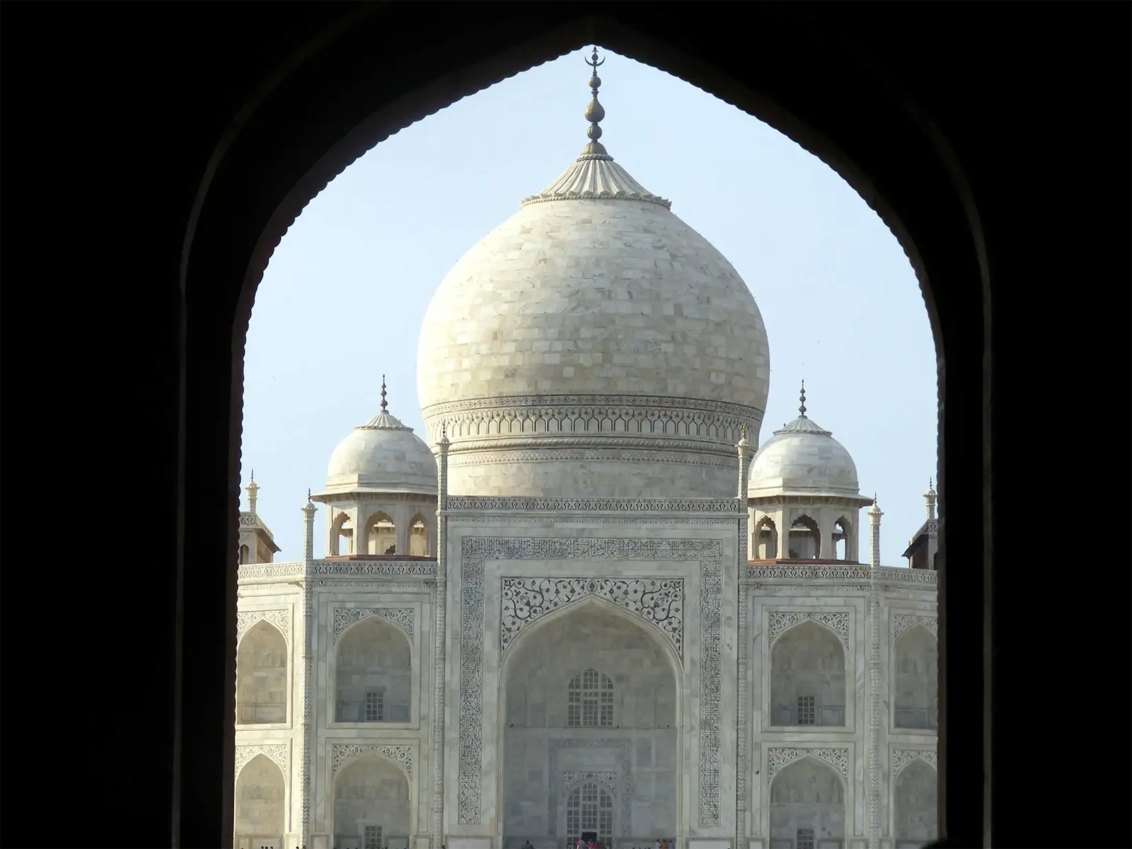 Le dôme du Taj Mahal encadré par l’arche sombre de sa porte d’entrée, à Agra