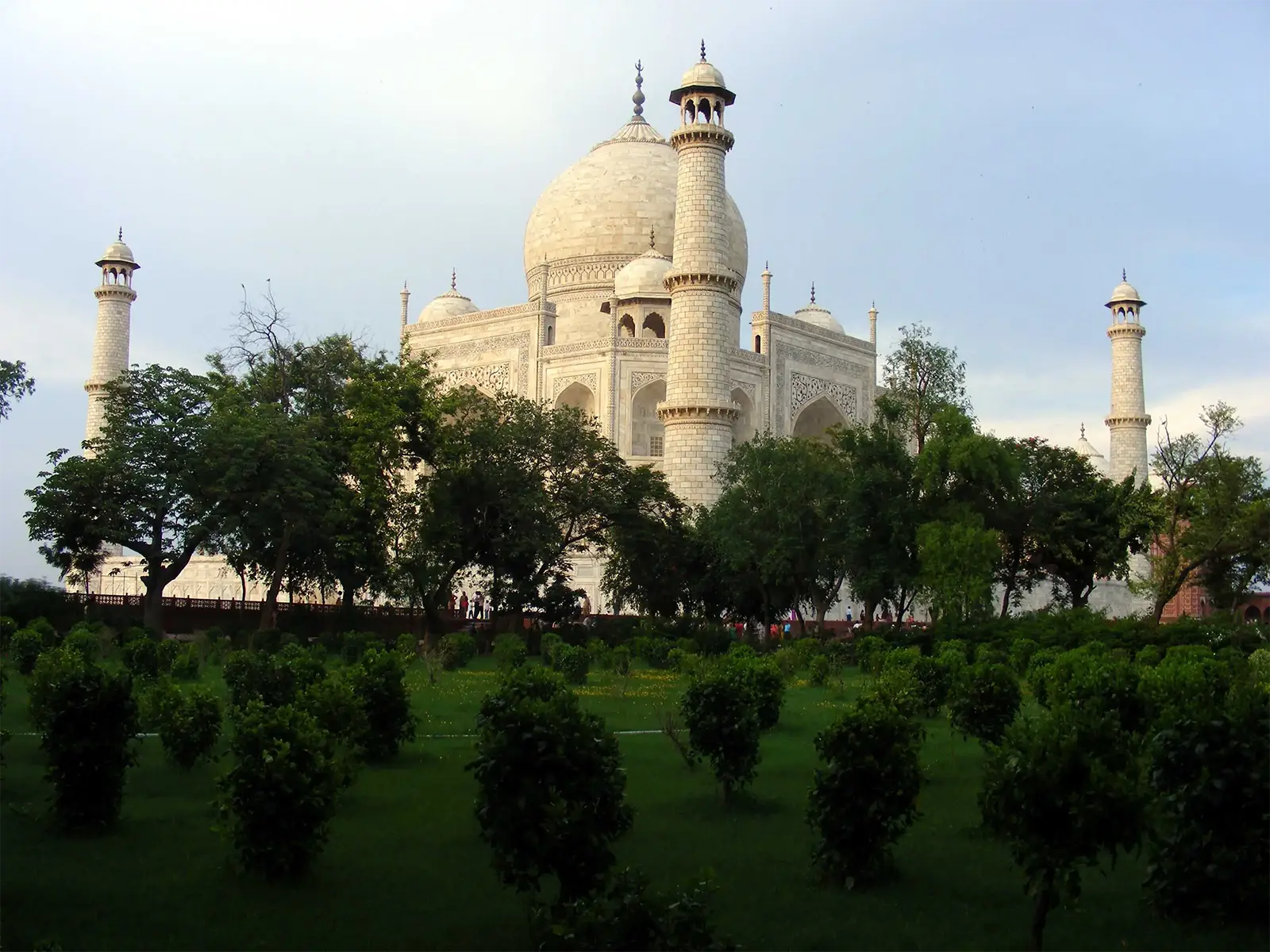 Le Taj Mahal derrière les arbres de ses jardins, sous un ciel nuageux à Agra