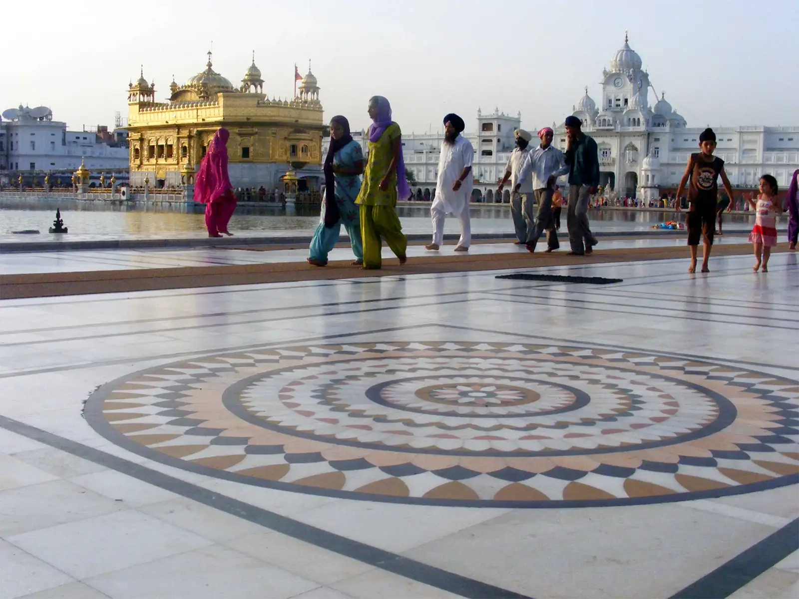 Pèlerins marchant sur le parvis de marbre en mosaïque autour du Temple d’Or d’Amritsar