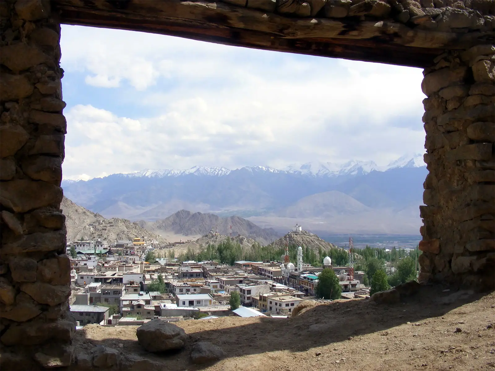 Leh et les sommets enneigés du Ladakh encadrés par une fenêtre de pierre en ruine