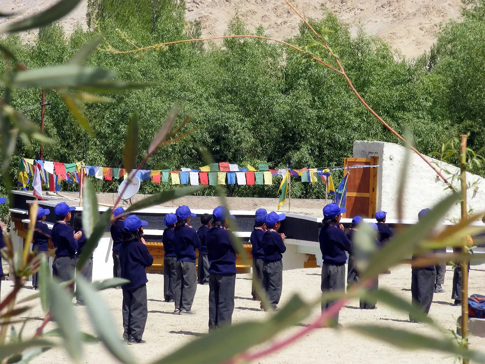 Écoliers en uniforme bleu alignés sous les drapeaux de prière dans une école de Leh