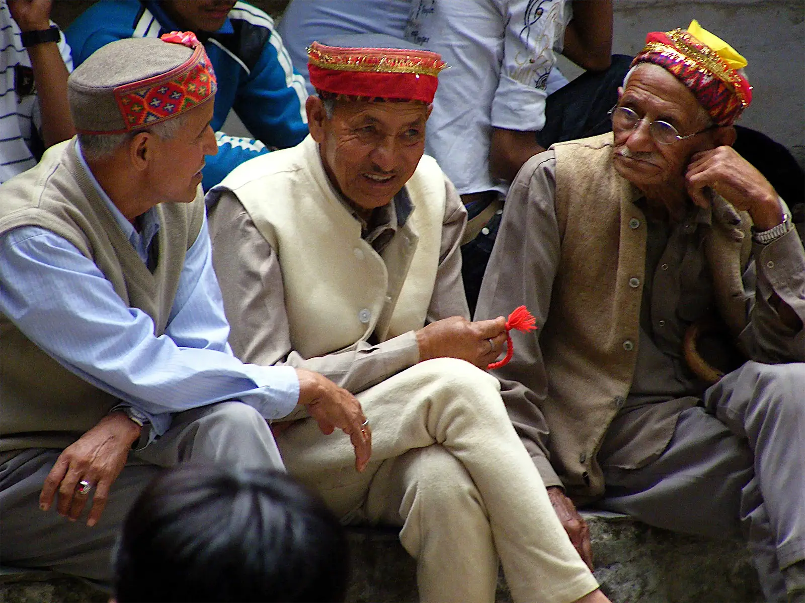 Trois hommes âgés en bonnet himachali brodé, assis lors d’une fête religieuse à Manali
