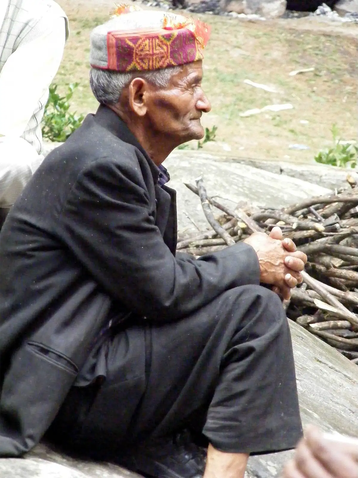 Vieil homme en bonnet himachali assis sur un rocher près d’un fagot de bois à Manali