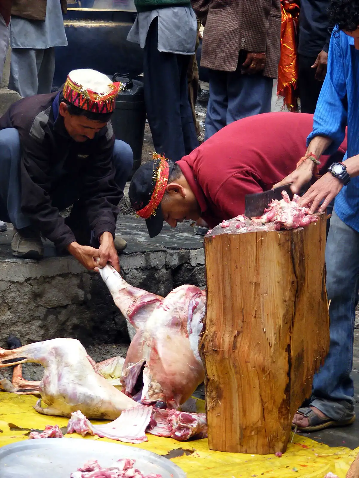 Homme en bonnet brodé découpant la viande au hachoir sur un billot, lors d’une fête à Manali