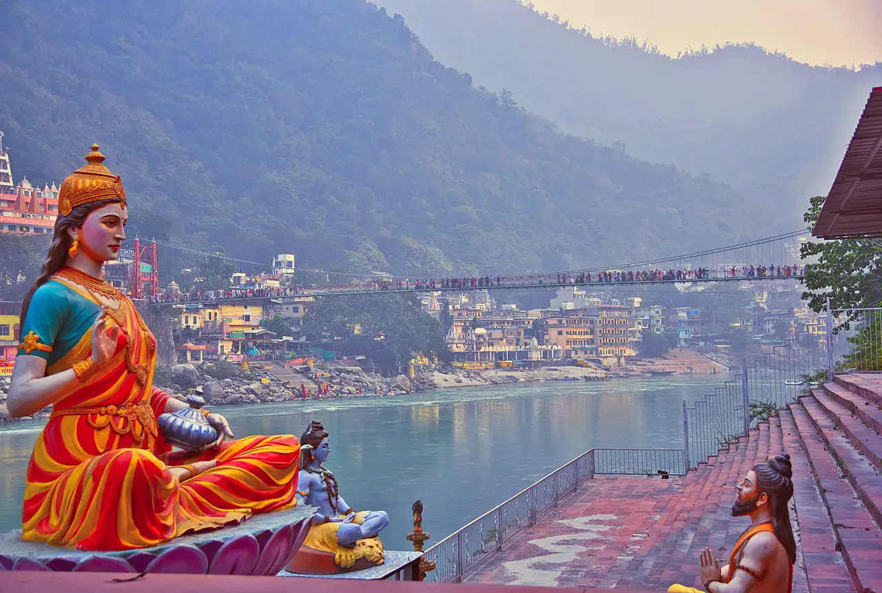 Statues de divinités hindoues face au Gange et à son pont suspendu, à Rishikesh