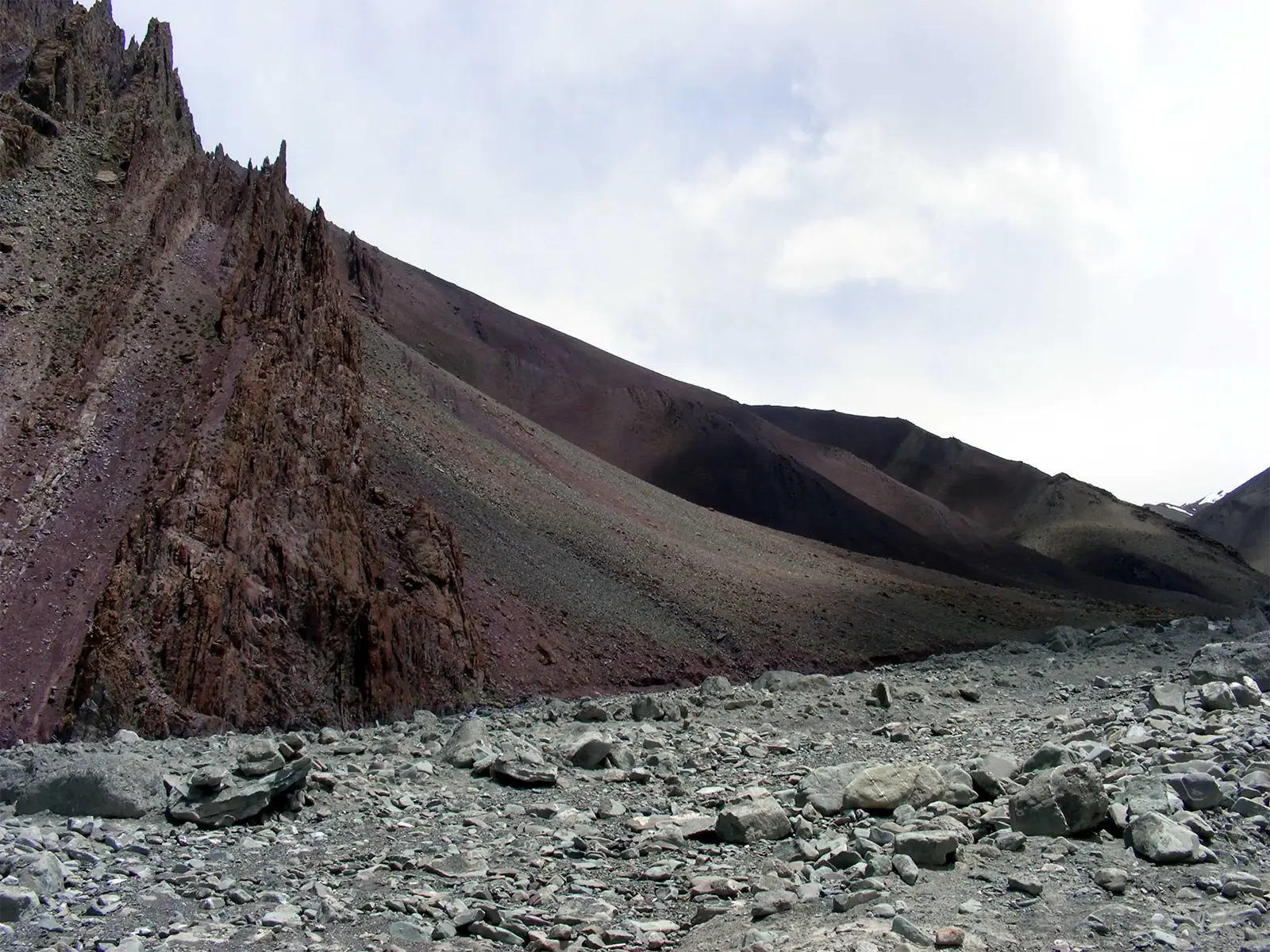 Arête rocheuse aux teintes pourpres dominant un lit de pierres sur le trek du Stok Kangri