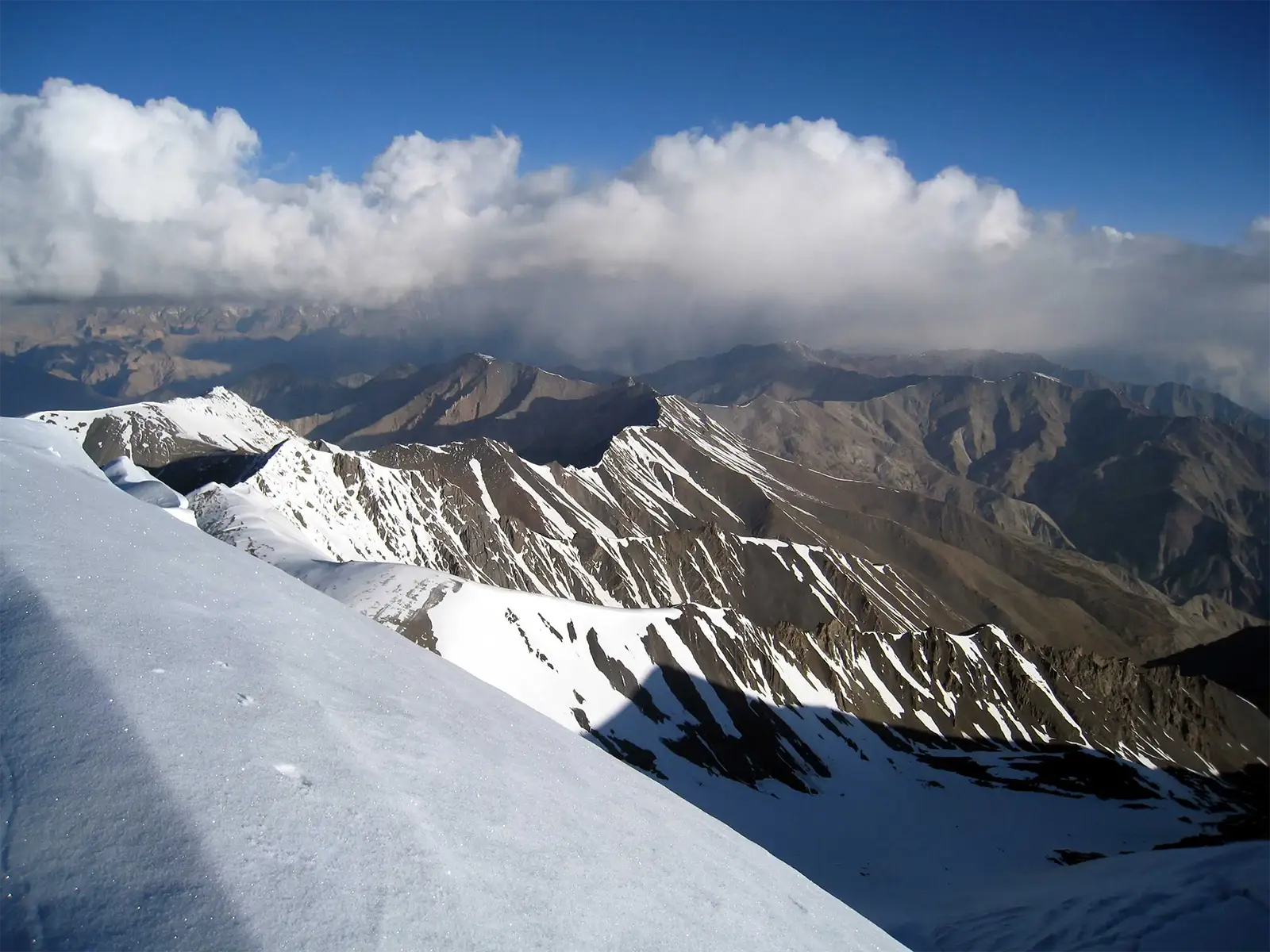 Pente de neige et crêtes striées de neige sous les nuages, près du sommet du Stok Kangri