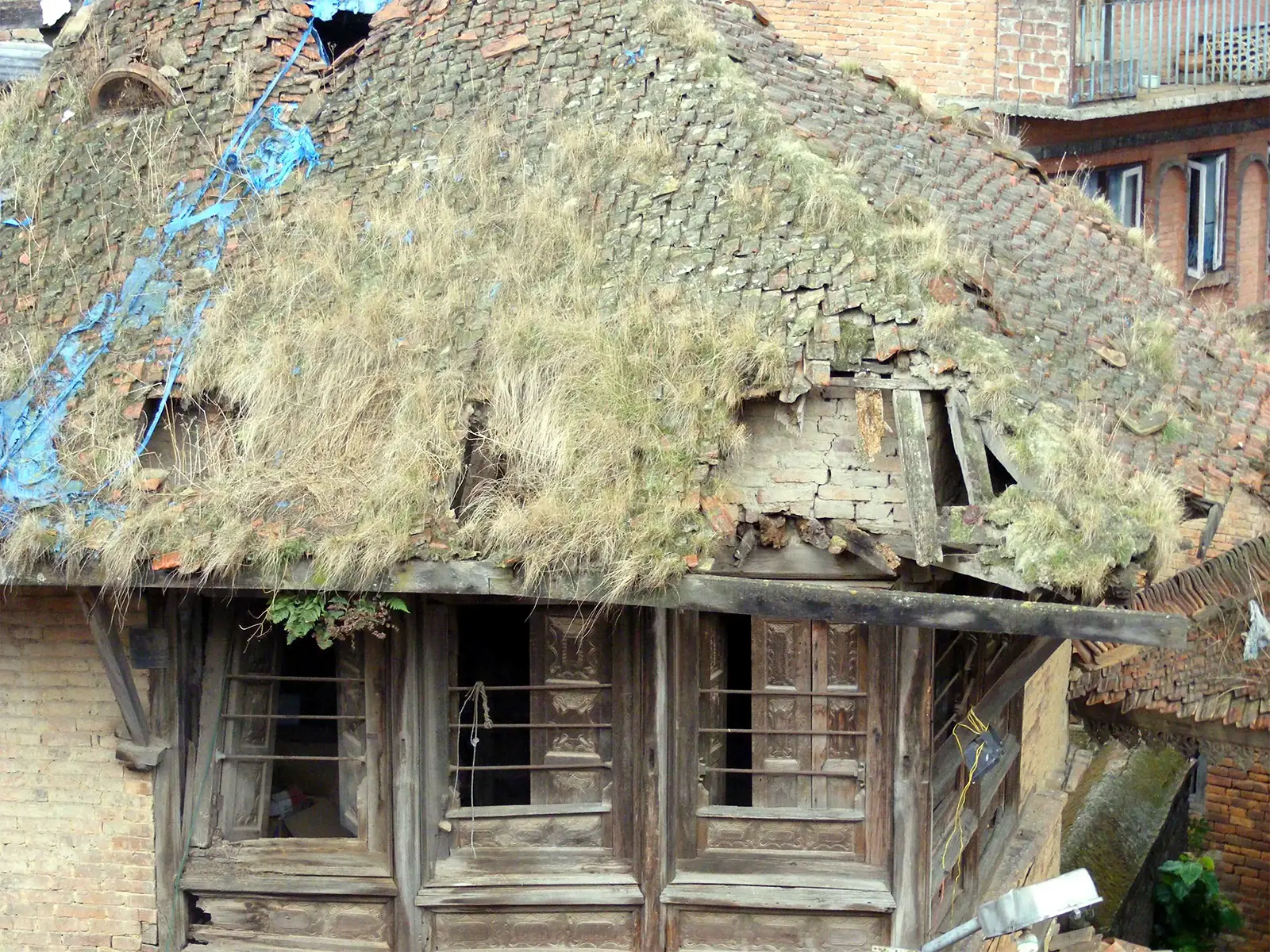 Vieille maison newar au toit de tuiles envahi d’herbes et aux fenêtres de bois à Bhaktapur