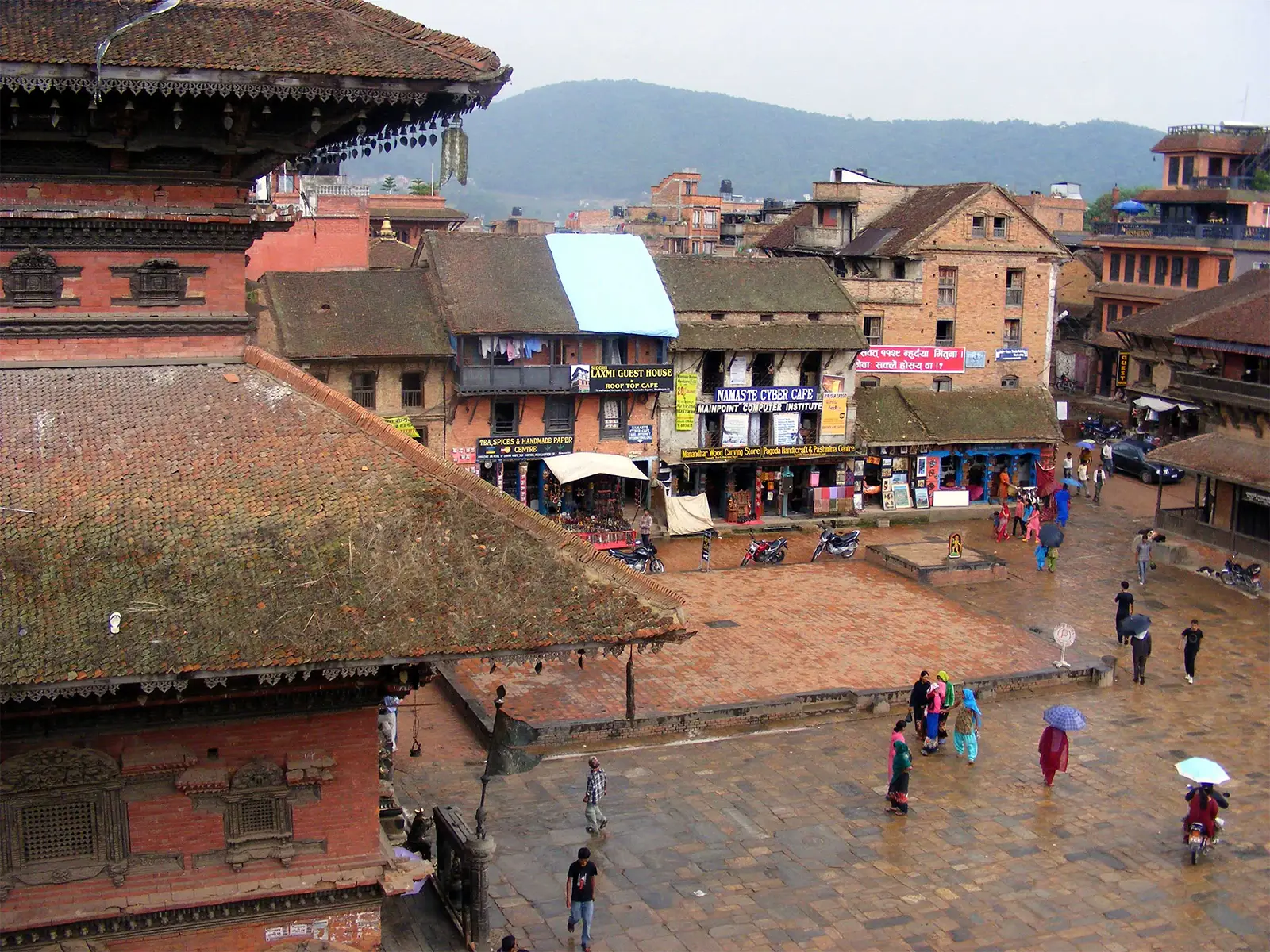 Place pavée de Bhaktapur sous la pluie, vue depuis le toit d’un temple, passants et parapluies
