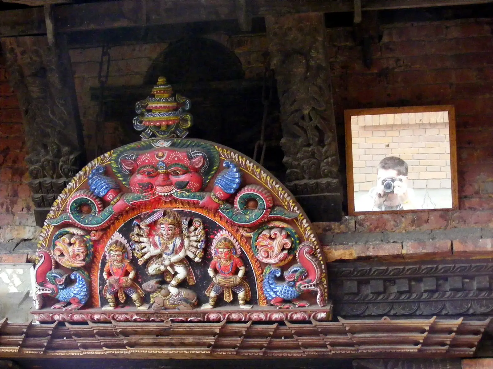 Torana en bois peint d’une divinité aux multiples bras, un voyageur dans le miroir, à Bhaktapur