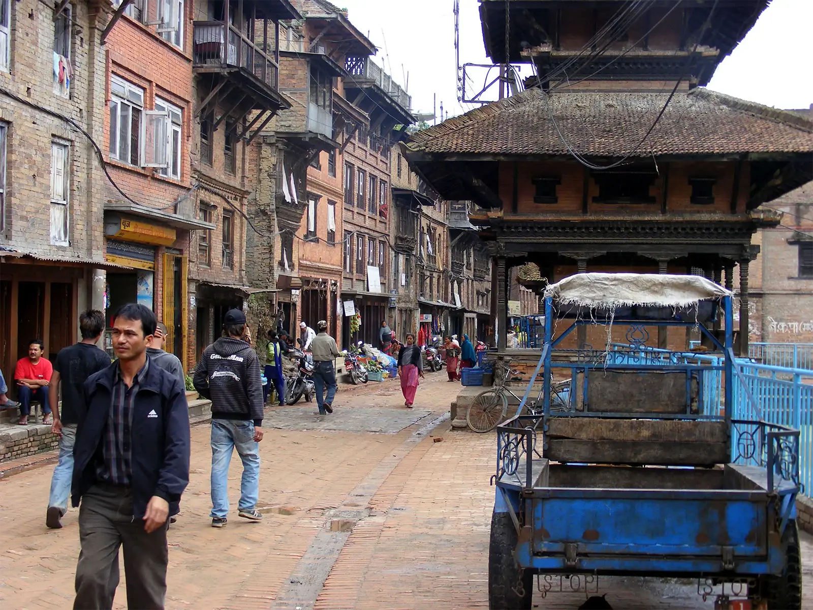 Rue pavée de briques, passants et pavillon de temple en bois à Bhaktapur