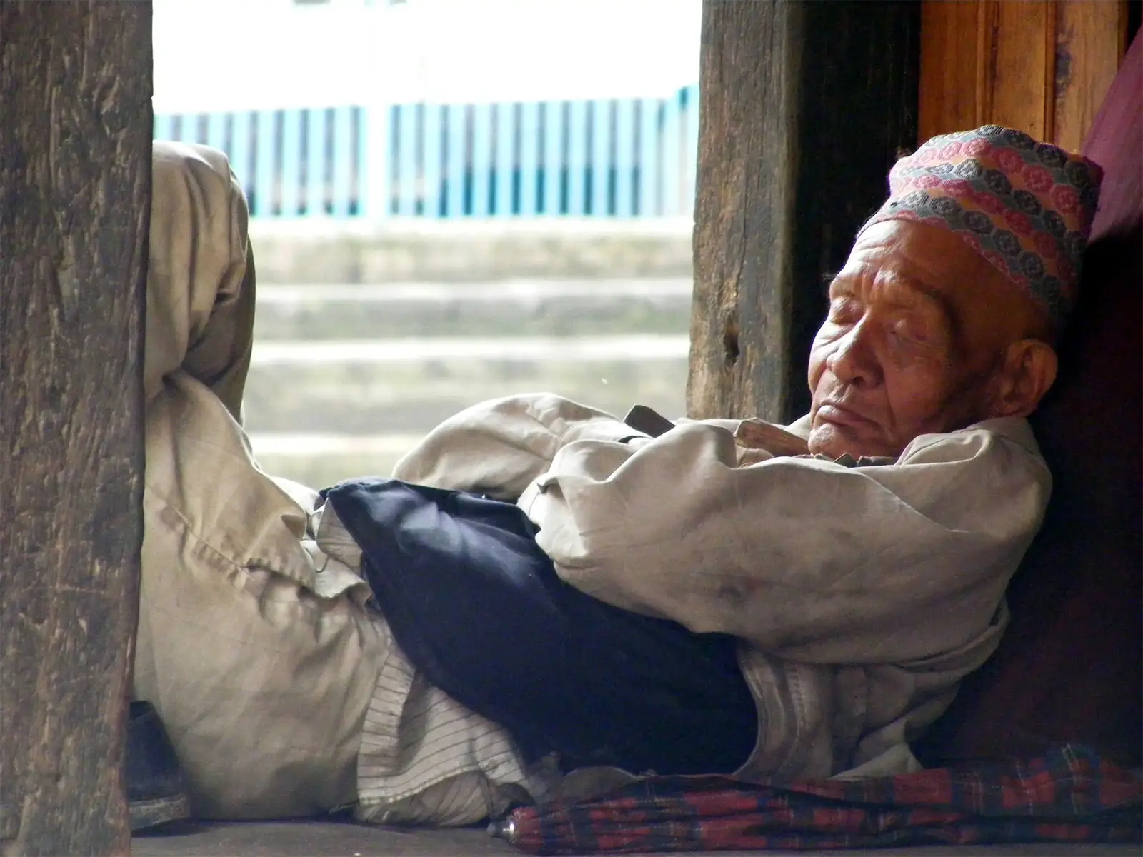 Vieil homme coiffé d’un topi faisant la sieste sous un porche en bois à Bhaktapur