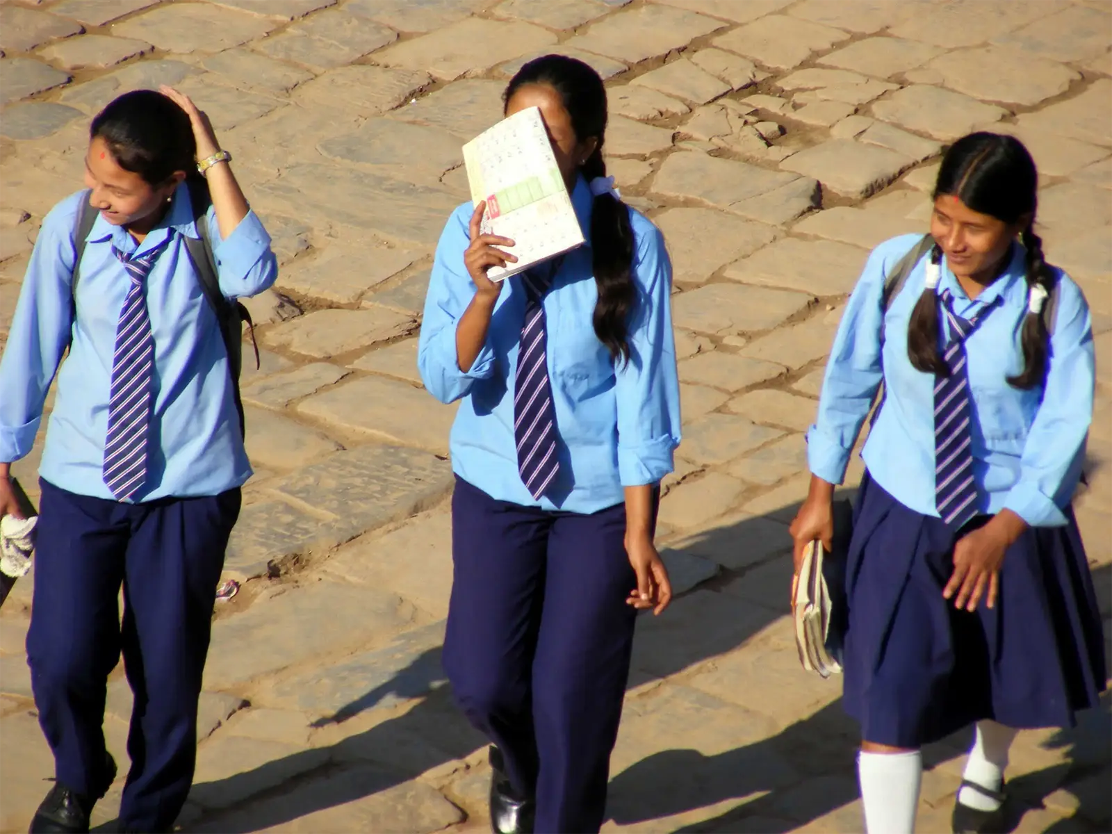 Trois écolières en uniforme bleu et cravate rayée marchant sur les pavés de Bhaktapur