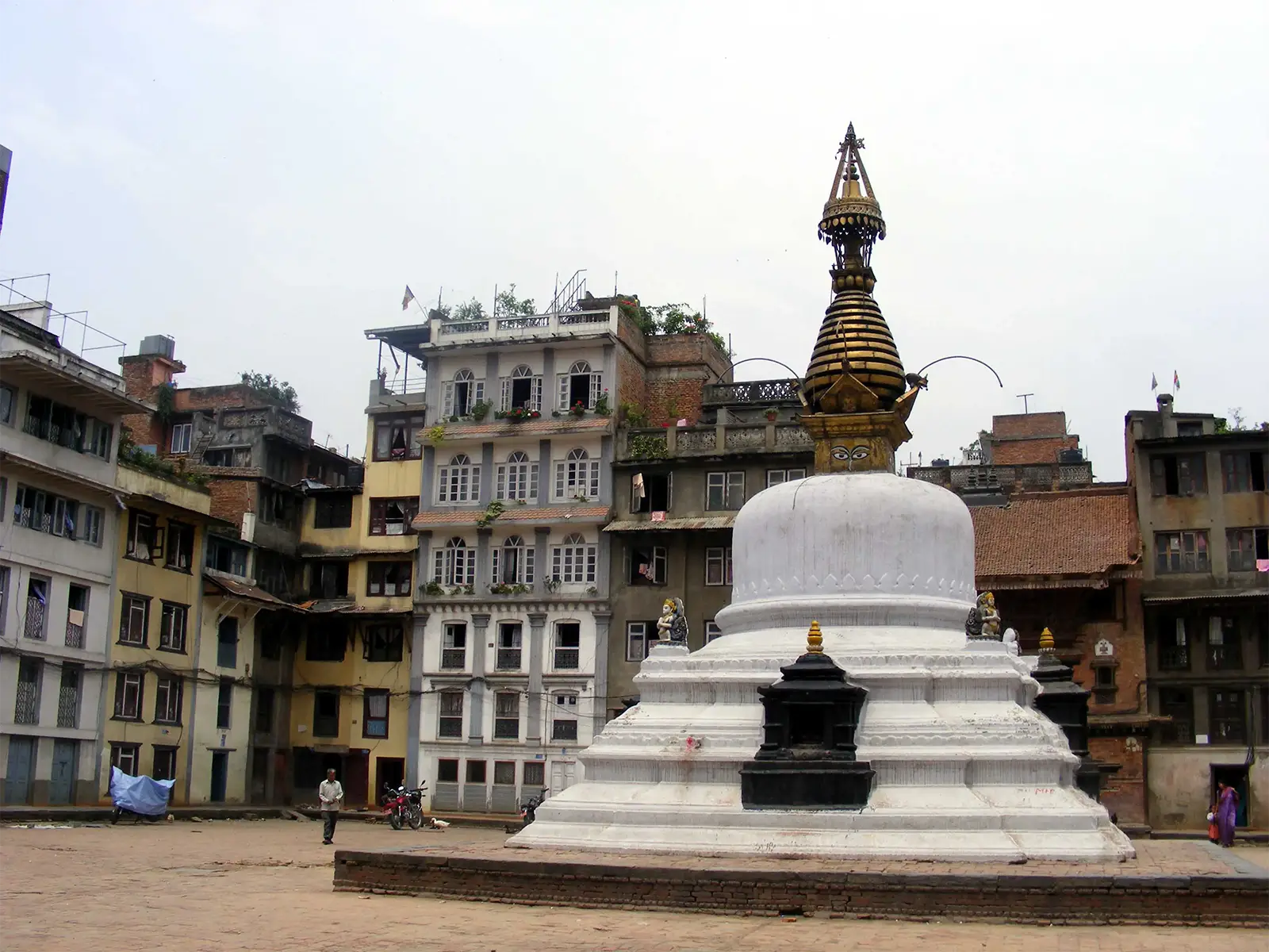 Stupa blanc à la flèche dorée au milieu d’une place entourée d’immeubles à Katmandou