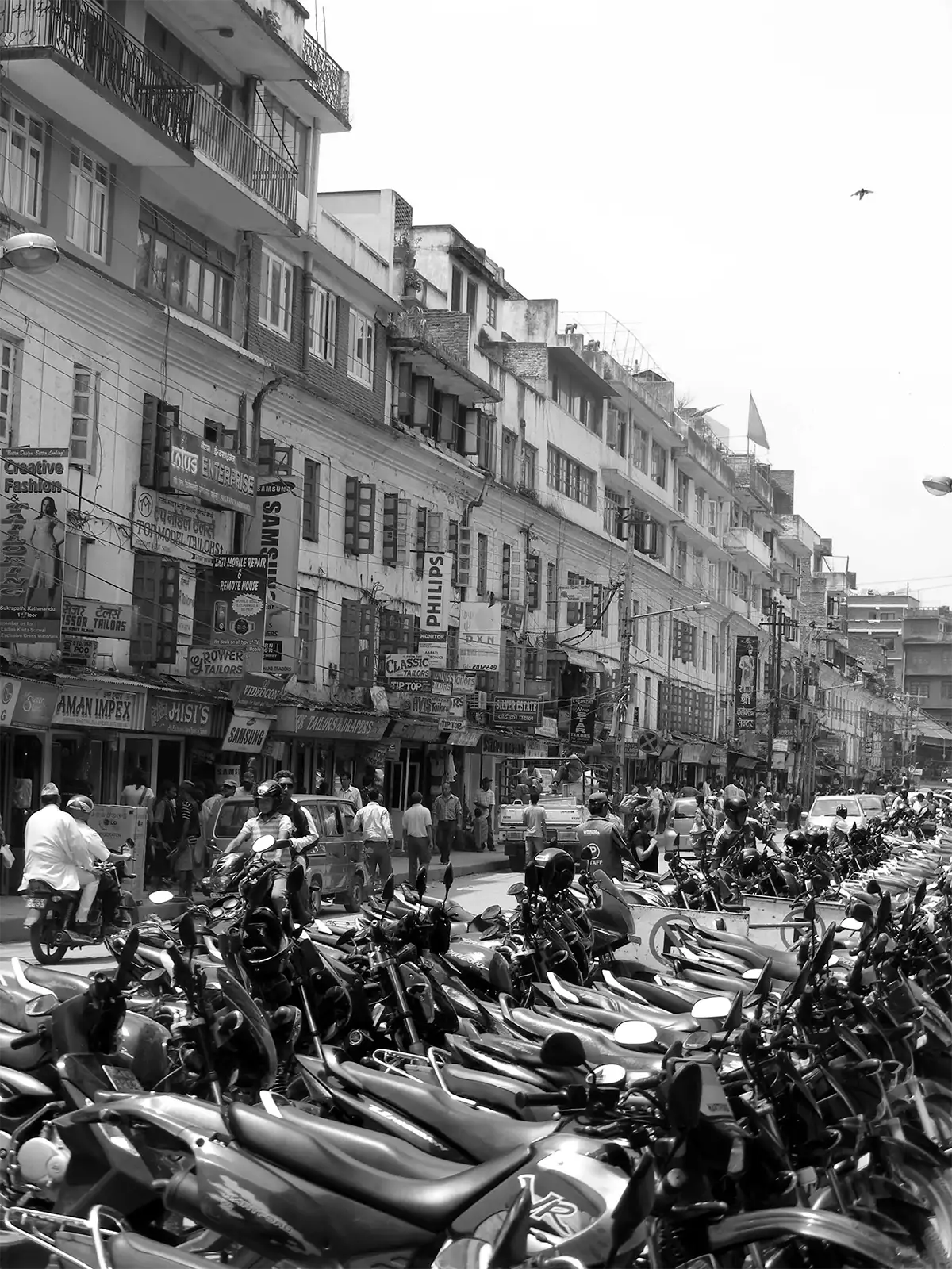 Rue commerçante de Katmandou en noir et blanc, bordée de motos garées