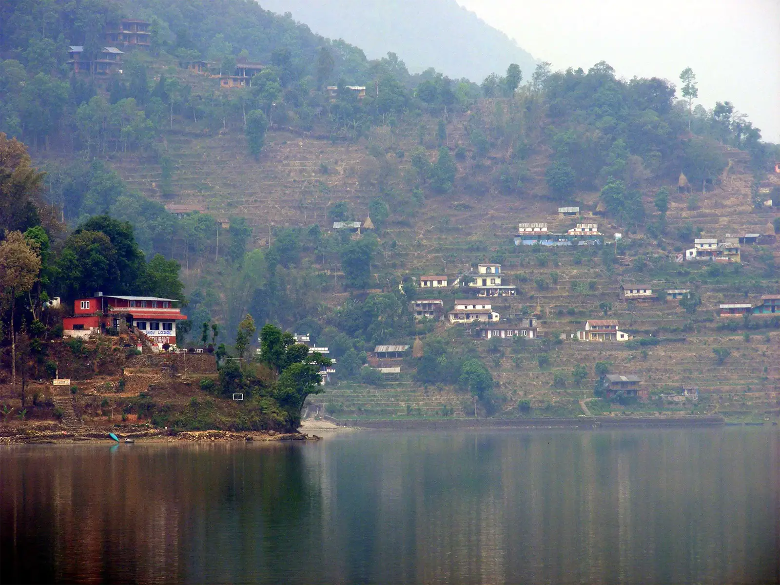 Collines en terrasses et maisons se reflétant dans un lac, près de Pokhara