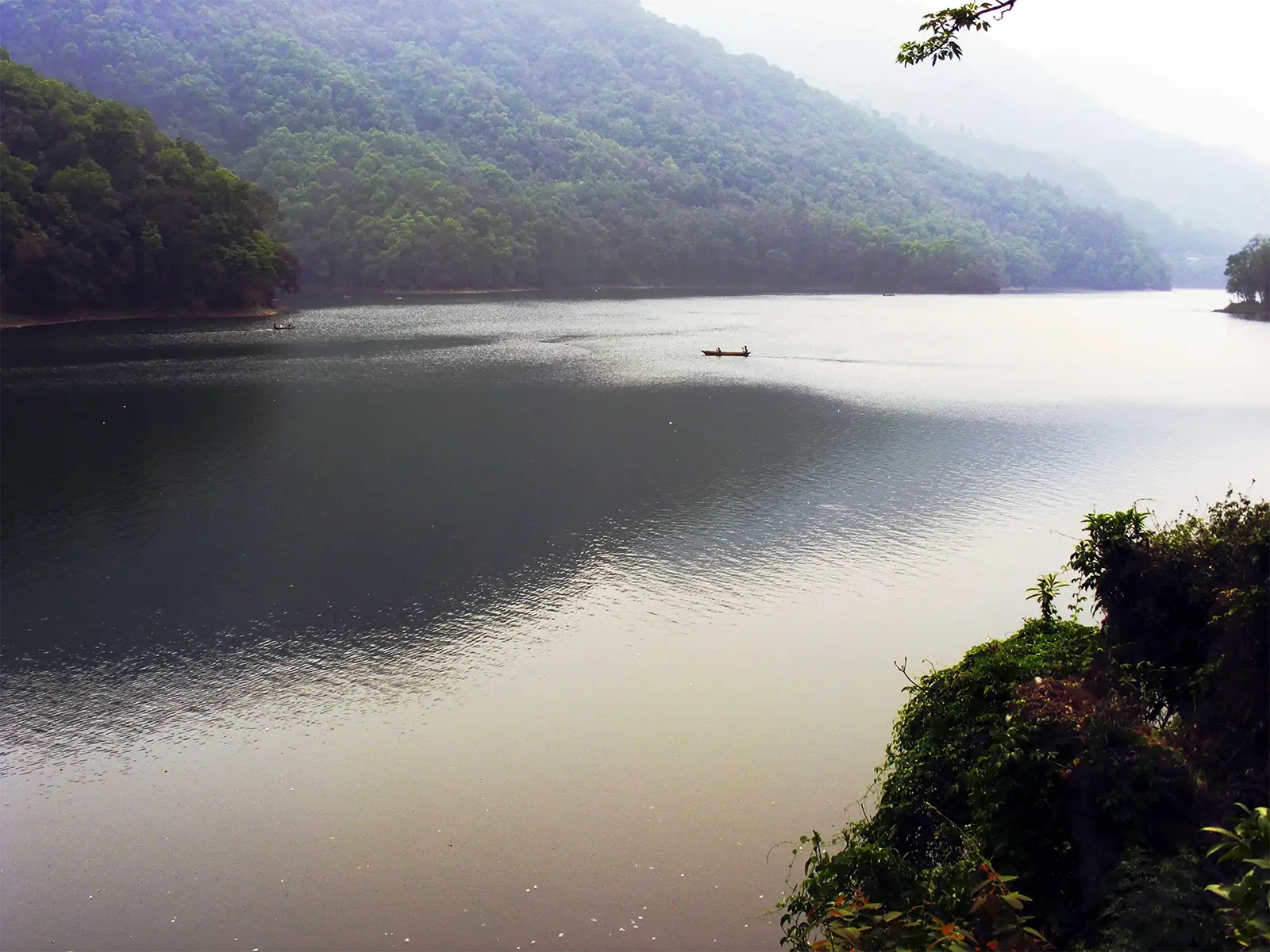 Canoë solitaire sur les eaux calmes du lac Phewa à Pokhara, entre les collines boisées