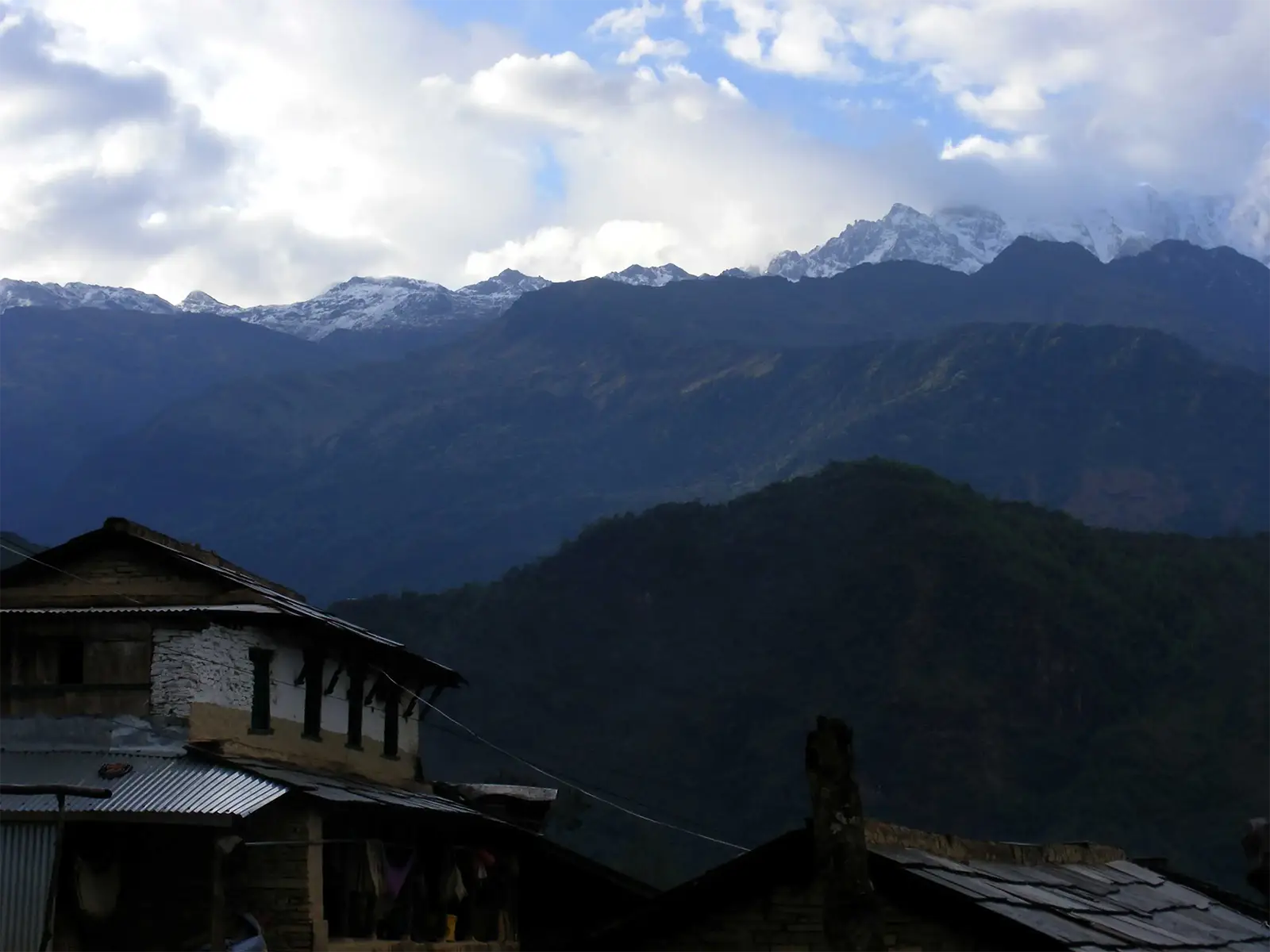 Sommets enneigés au-dessus des crêtes boisées et toits d’un village du trek des Annapurnas