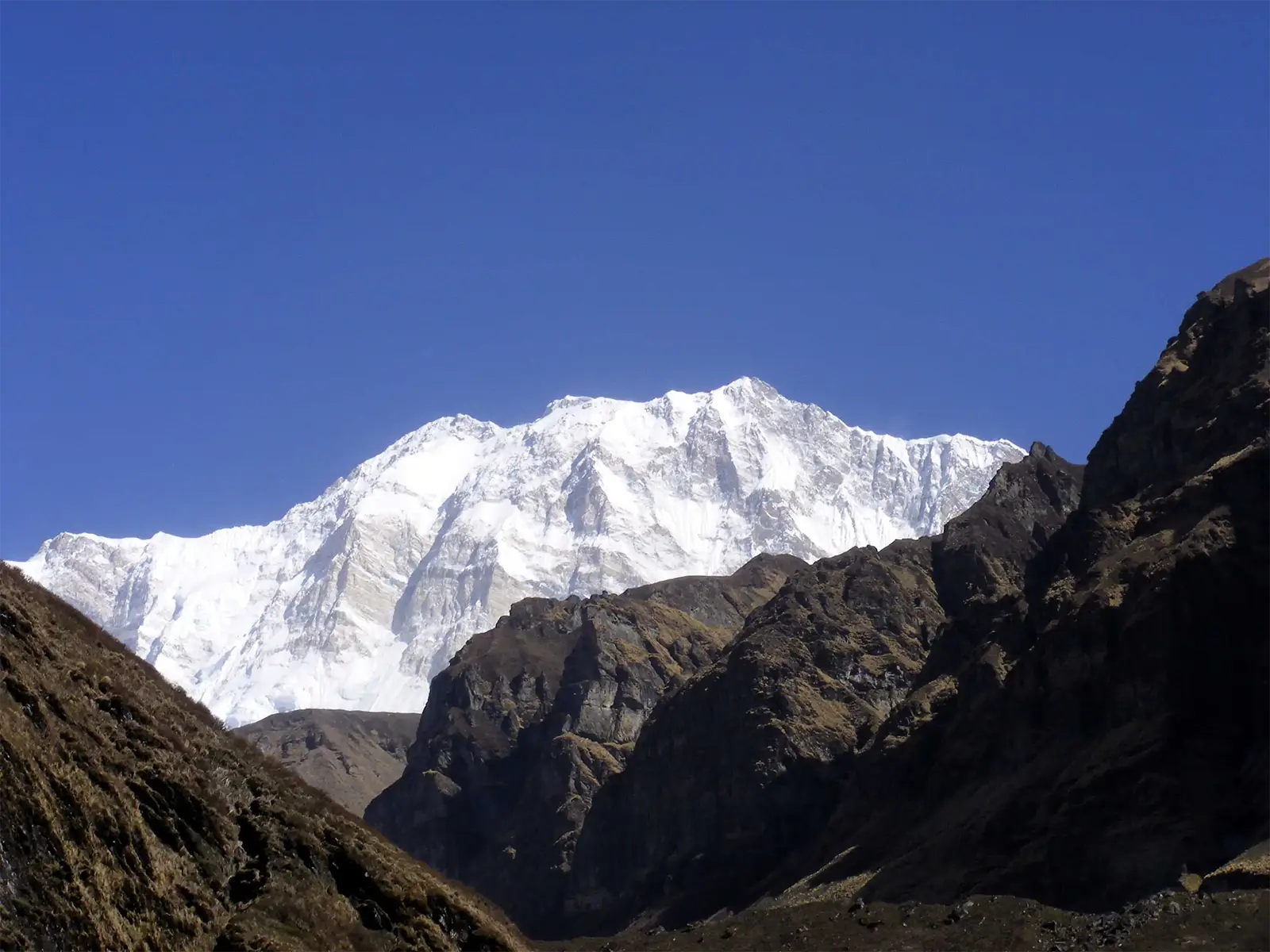 Massif enneigé des Annapurnas sous un ciel bleu intense, derrière des crêtes rocheuses