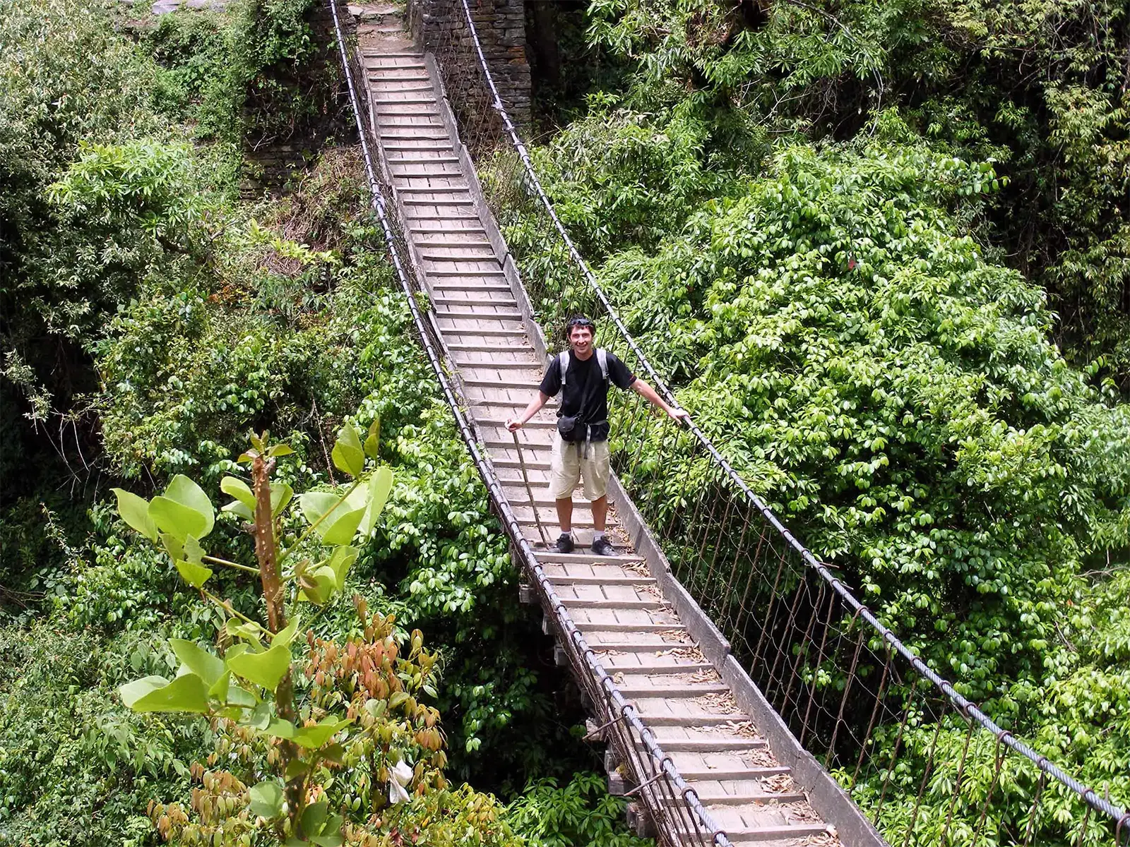 Un voyageur sur une passerelle suspendue au-dessus de la jungle, sur le trek des Annapurnas
