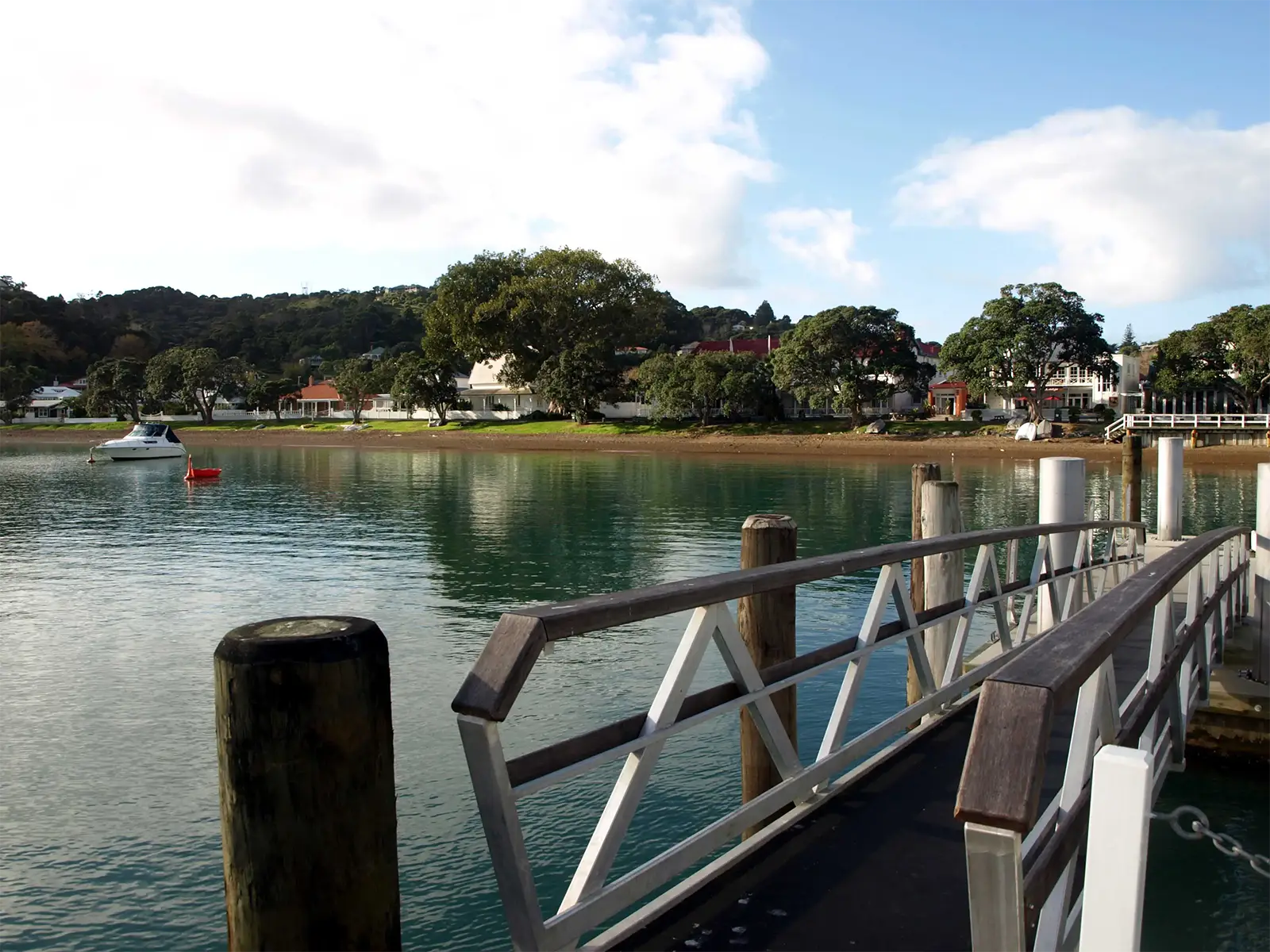 Ponton en bois et front de mer arboré d’un village de la Bay of Islands, sur une eau calme