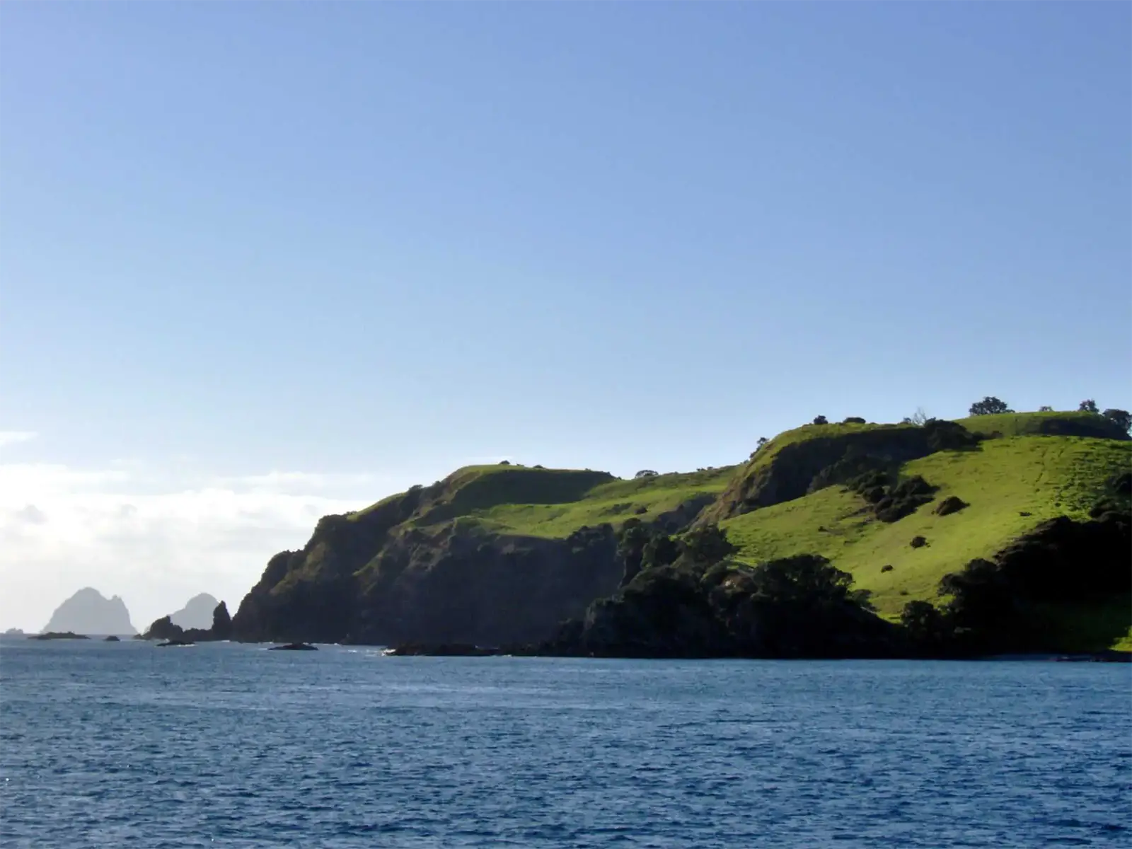 Promontoire herbeux et pitons rocheux au large, vus du bateau dans la Bay of Islands