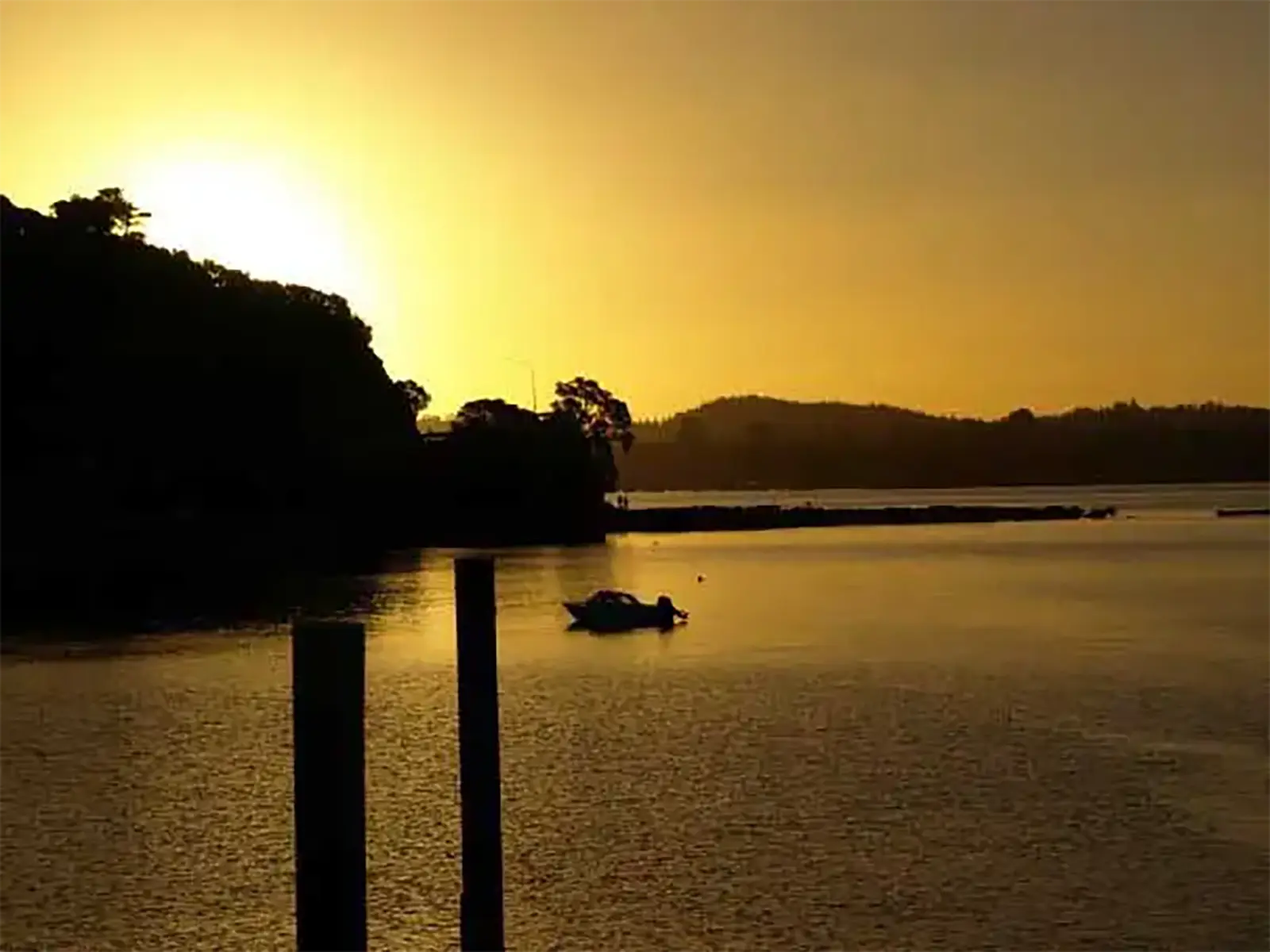 Coucher de soleil doré sur la baie, avec un bateau et des pieux de ponton en silhouette, à Paihia