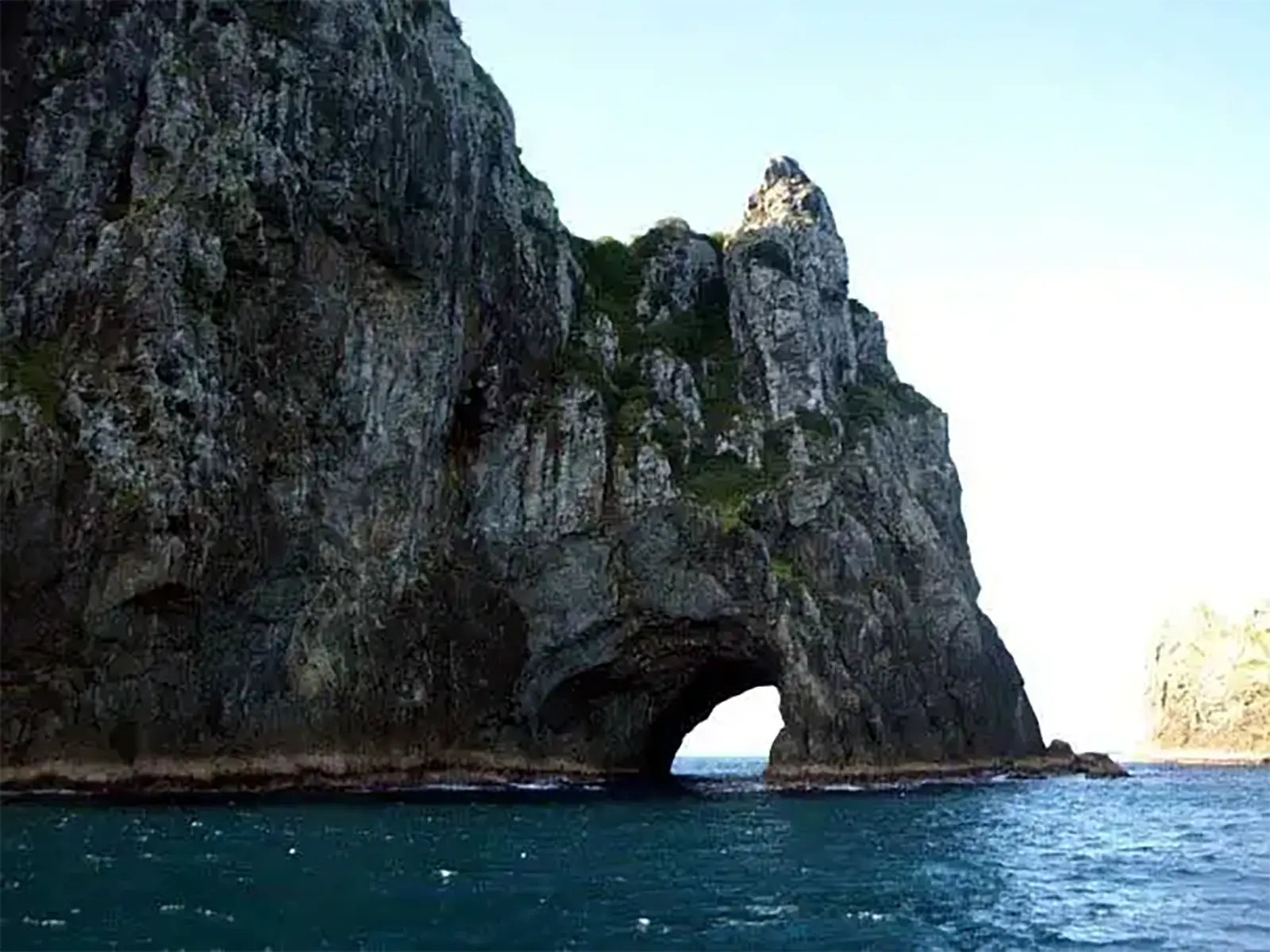 L’arche du Hole in the Rock vue de profil depuis le bateau, entre falaise grise et mer turquoise