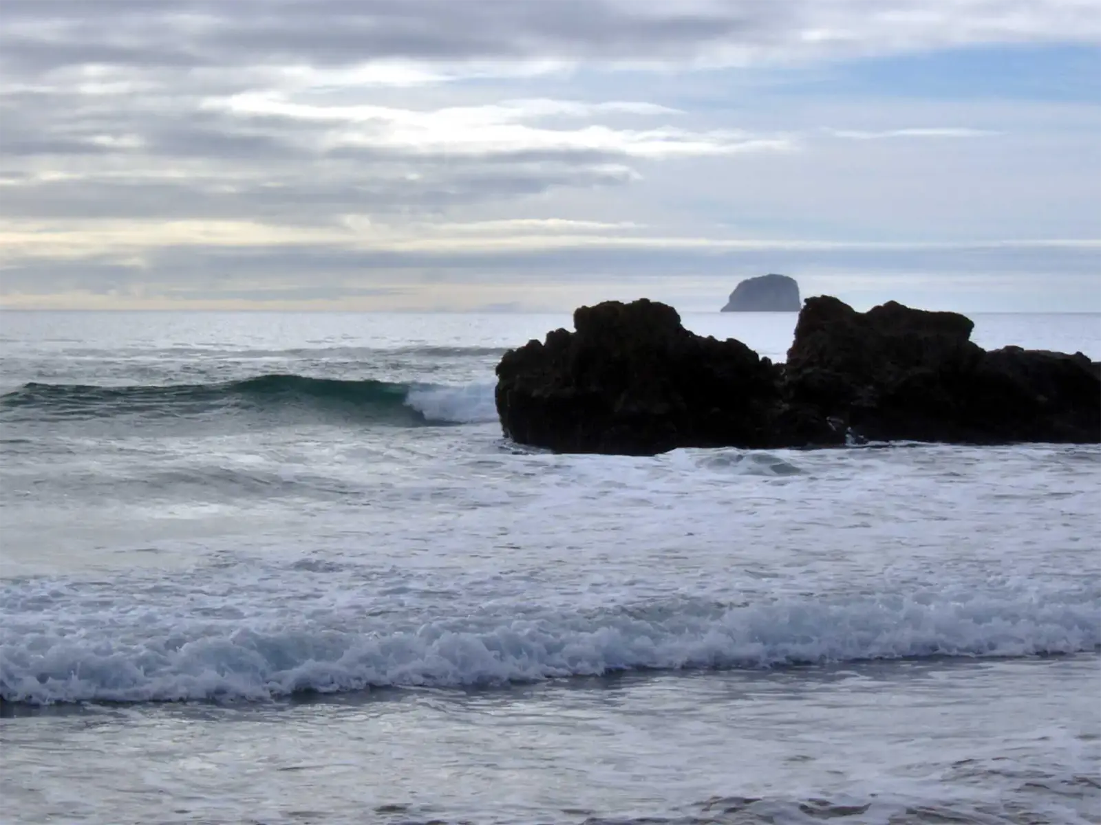 Vagues se brisant sur des rochers noirs face à un îlot au large de la péninsule de Coromandel