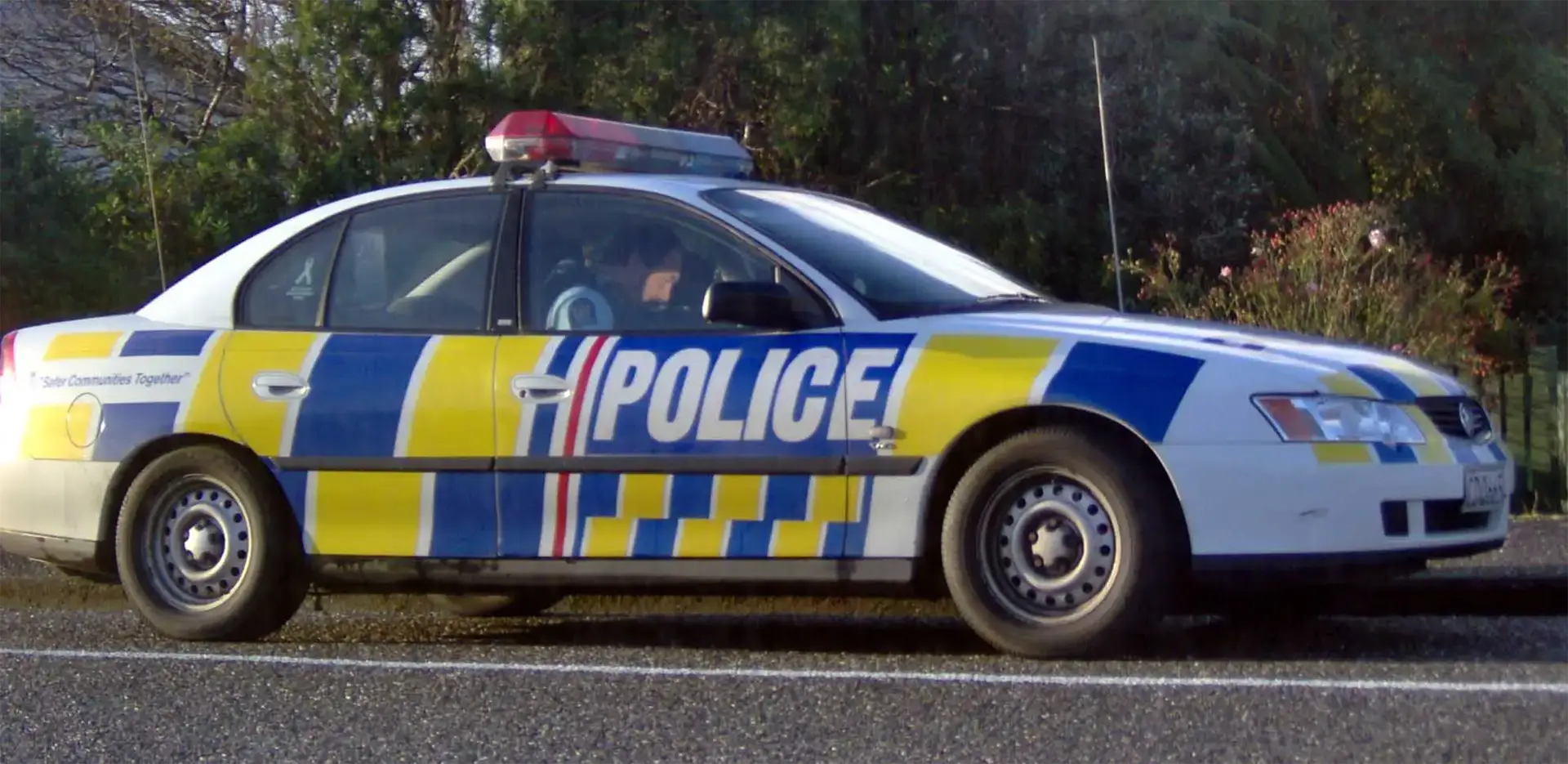 Voiture de police néo-zélandaise aux damiers bleus et jaunes garée au bord de la route vers Greymouth
