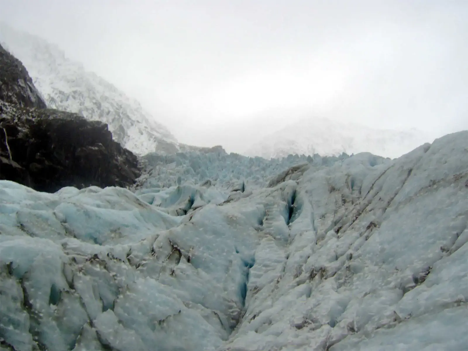 Champ de séracs du glacier Fox sous les sommets enneigés noyés dans la brume