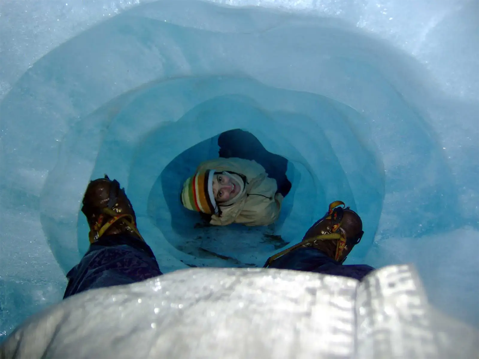 Un randonneur au bonnet rayé au bout d’un tunnel de glace bleue dans le glacier Fox