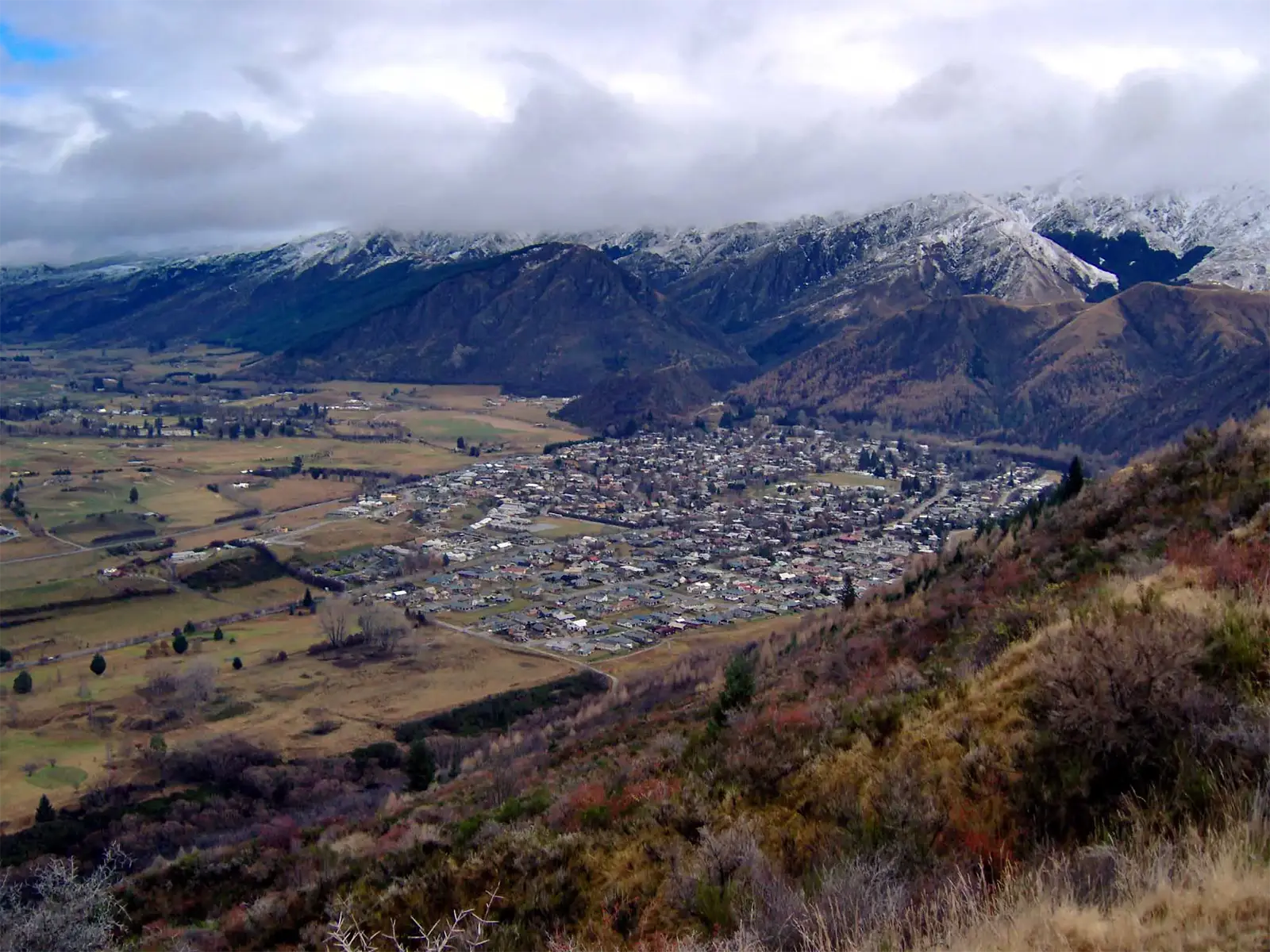 Petite ville nichée dans une vallée au pied de montagnes enneigées, vue des collines près de Queenstown
