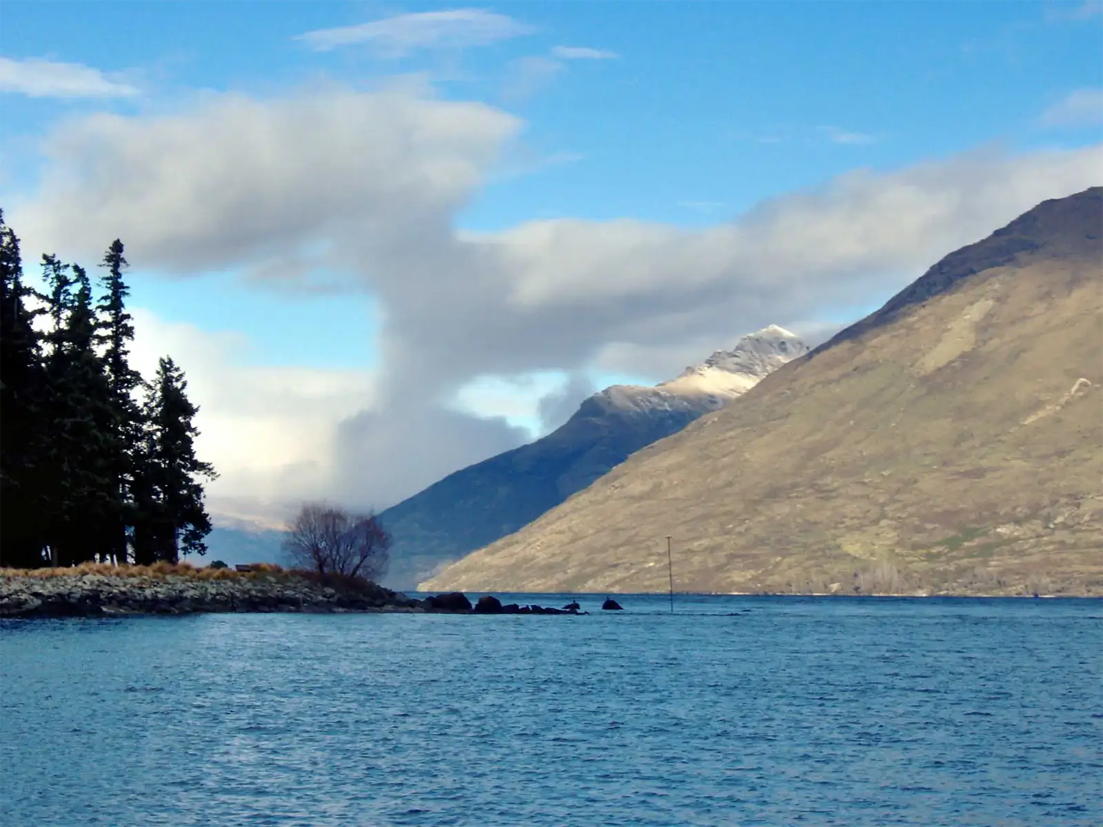 Le lac Wakatipu et ses montagnes sous un ciel bleu traversé de nuages, près de Queenstown