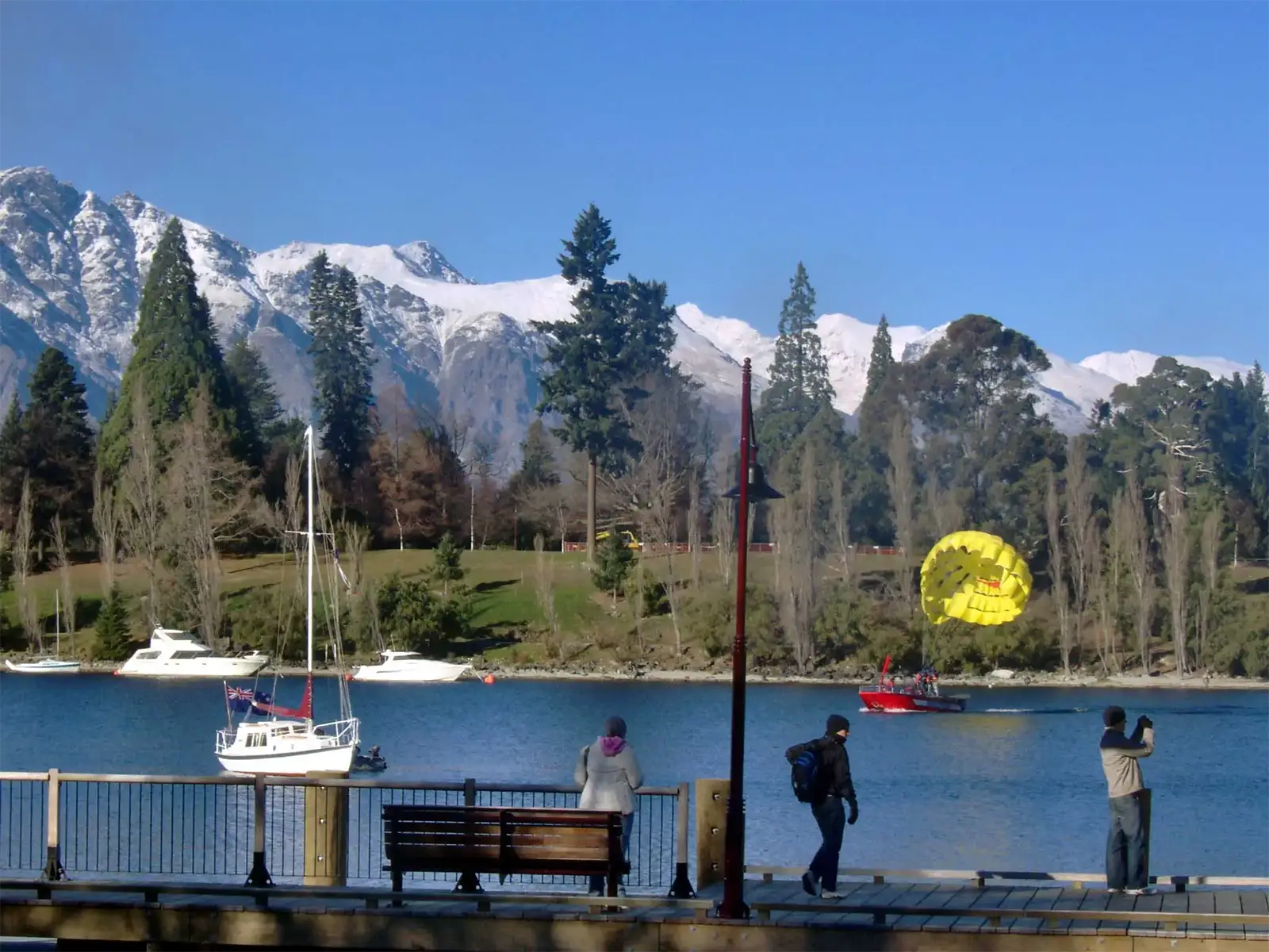 Parachute ascensionnel jaune sur le lac Wakatipu, face aux sommets enneigés de Queenstown