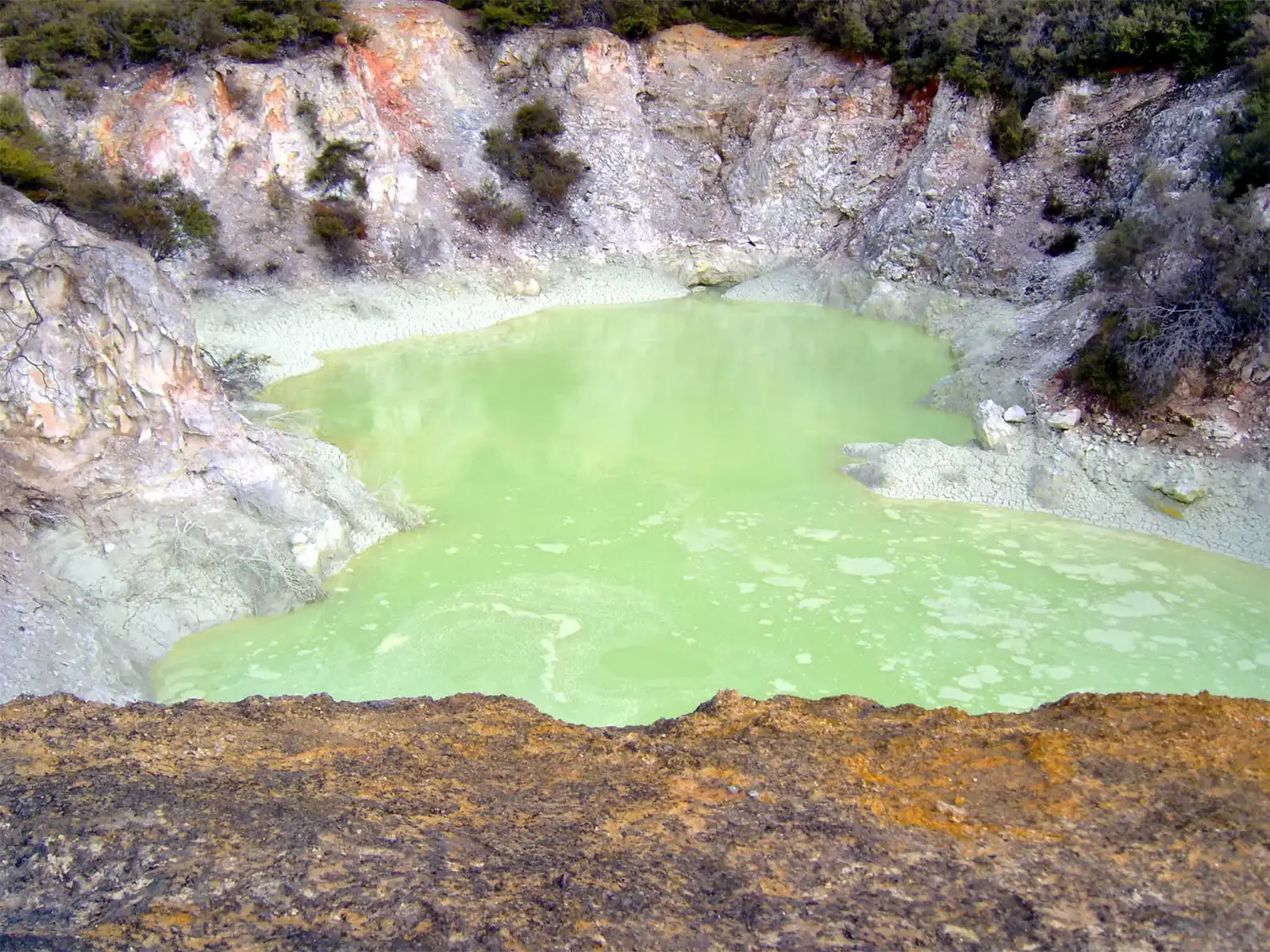 Bassin géothermique d’un vert fluo au pied de parois ocre, dans la région de Rotorua