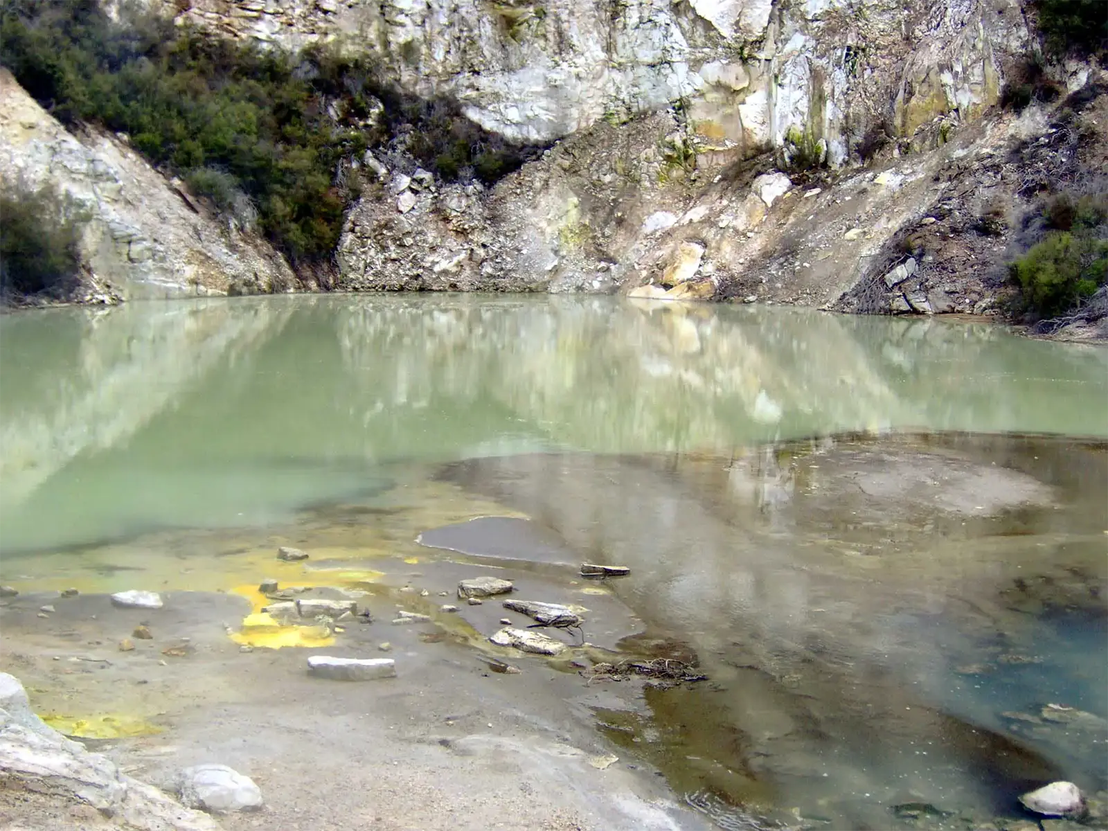 Lac géothermique laiteux et dépôts de soufre jaune au pied d’une falaise blanche, près de Rotorua