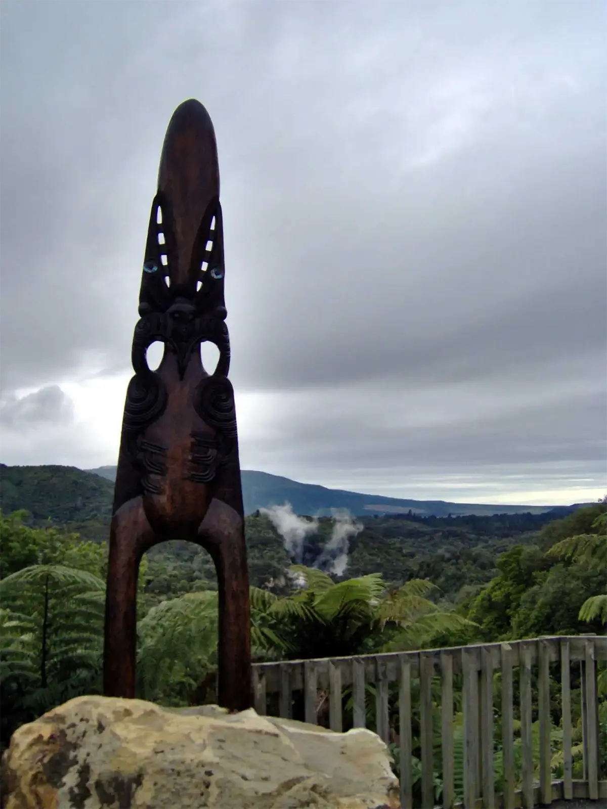 Sculpture maorie en bois au-dessus d’une vallée fumante et de fougères, sur un belvédère près de Rotorua