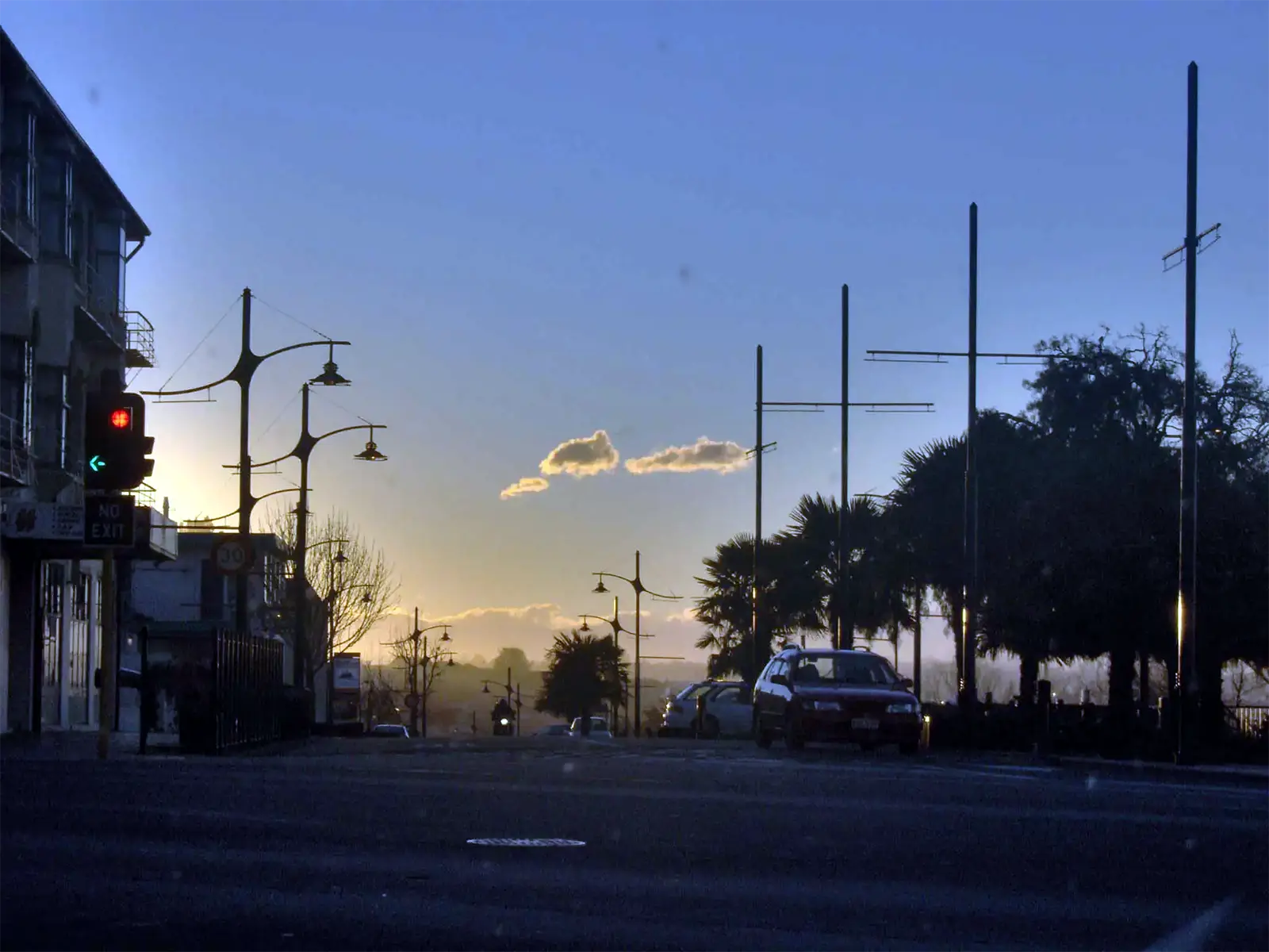 Rue de Timaru bordée de palmiers et de réverbères à contre-jour au coucher du soleil, sur la côte est de l’île du Sud